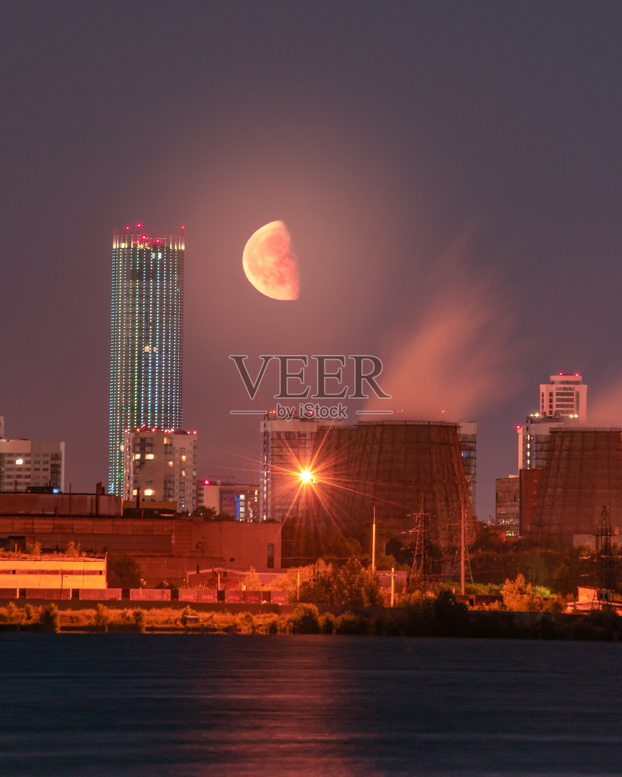 半月从叶卡捷琳堡市的摩天大楼和工业厂房后面升起照片摄影图片