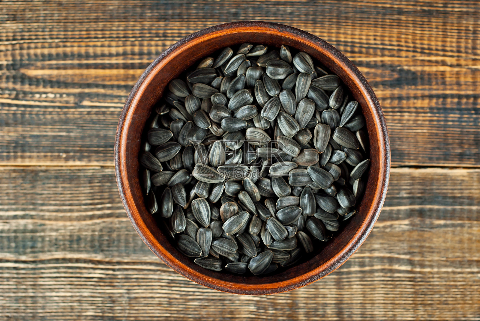 葵花籽放在破旧的木板上的泥碗里。棕色的木桌上放着坚果。照片摄影图片