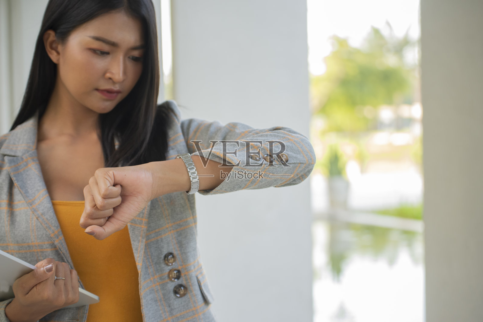 在办公室看手表检查时间的专业商人。年轻的商人看钟上班。桌上有日历、笔记本电脑、年度报告和总结报告。预约会议时间到。照片摄影图片