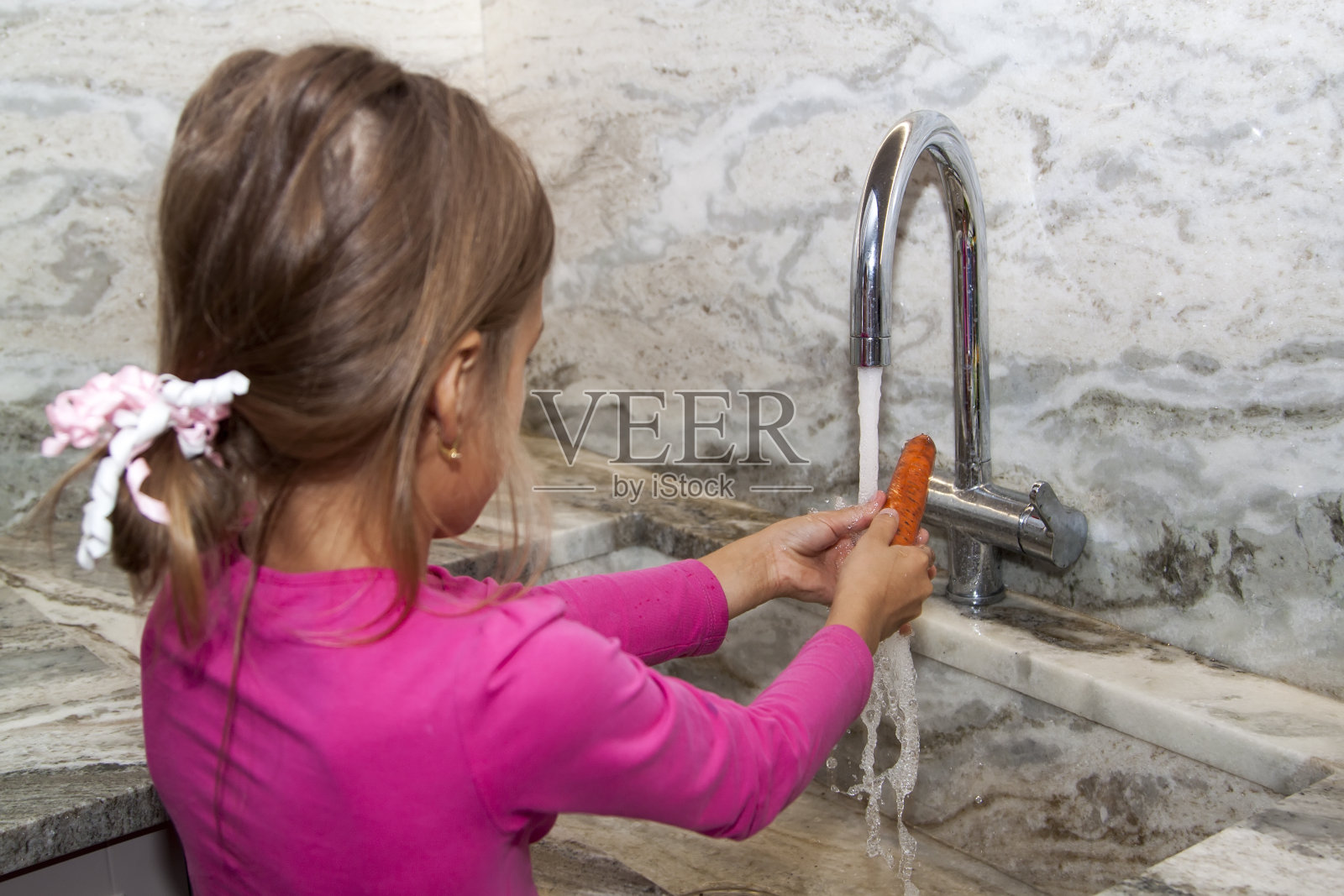小女孩在厨房的大理石水槽里洗胡萝卜。新鲜健康的儿童食品照片摄影图片
