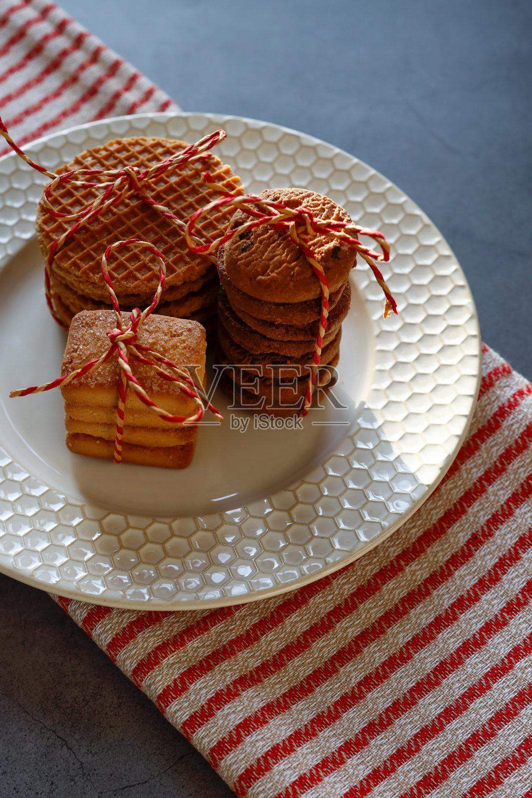 将饼干和焦糖华夫饼绑在米色盘子上，在红色米色条纹餐巾的黑色背景上照片摄影图片