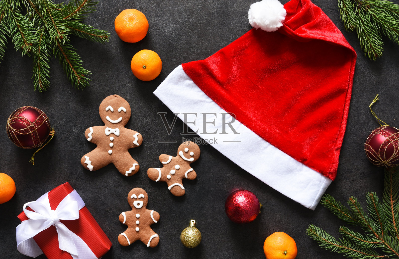 新年的装饰品有圣诞老人的帽子、橘子和姜饼放在新年的桌子上。布局。照片摄影图片