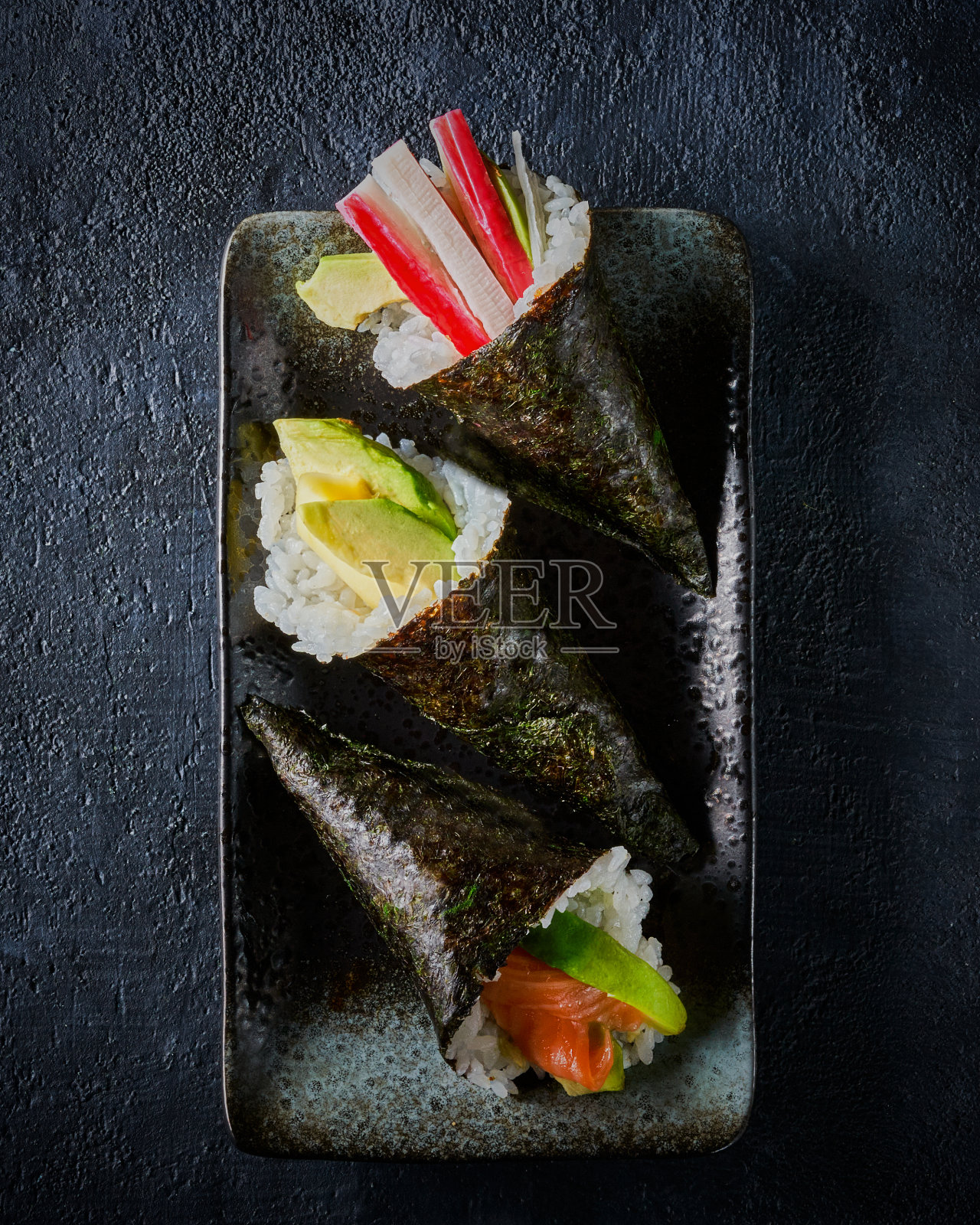 一套鲭寿司，三文鱼，金枪鱼，鳄梨，蟹棒在陶瓷盘子上的深色背景和复制空间。前视图。传统的日本料理。照片摄影图片