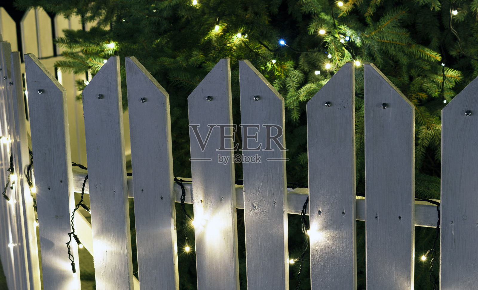 白色的木制栅栏，圣诞树周围挂着圣诞灯。照片摄影图片