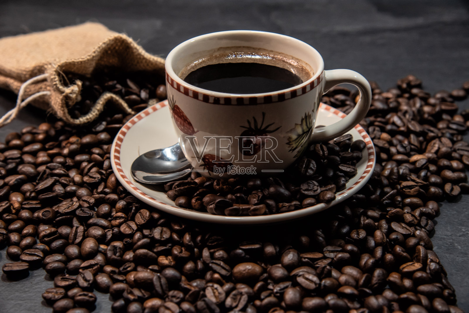 一杯被烤咖啡豆包围的咖啡和一个装满咖啡豆的麻袋。照片摄影图片