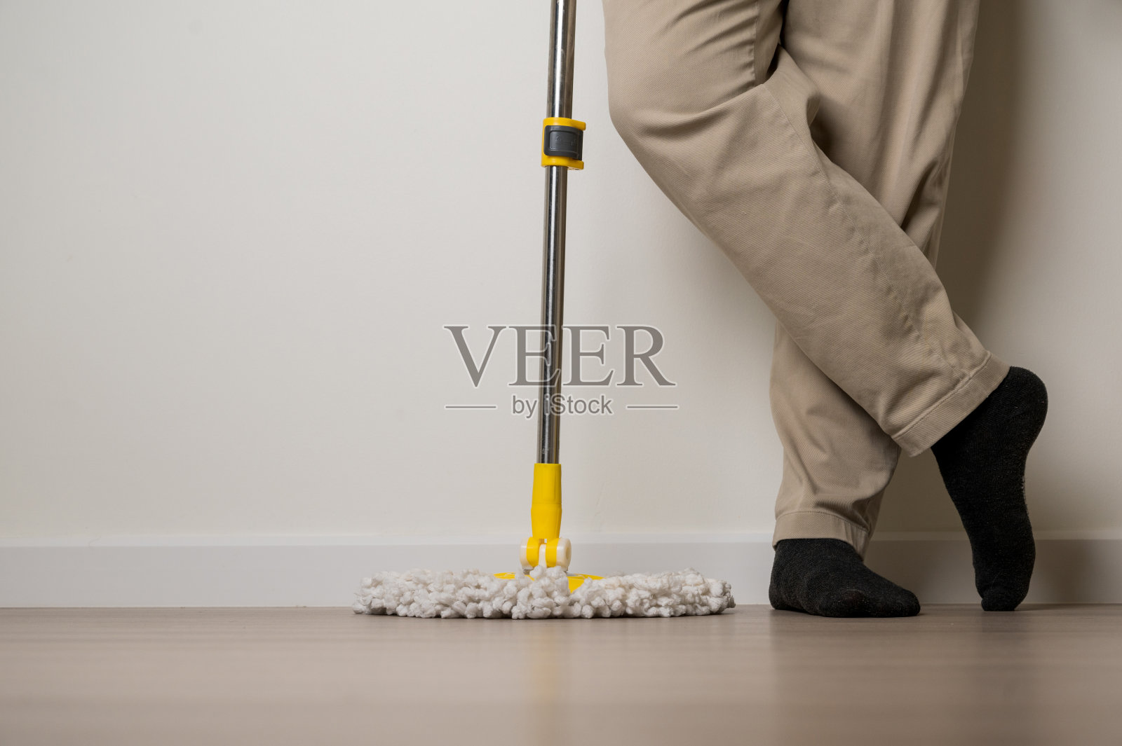男性站着点腿，拿着黄色拖把。他是专业打扫房间的。照片摄影图片