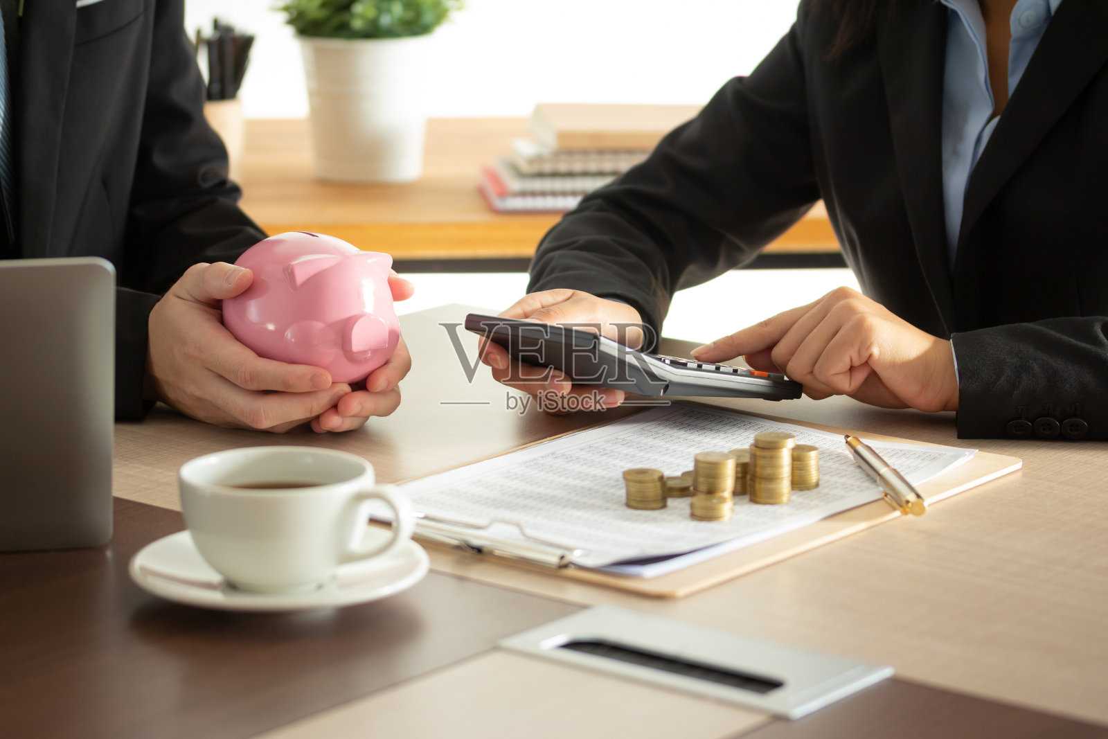 商人的手，粉红色的存钱罐，木桌子上的恒温器和硬币照片摄影图片