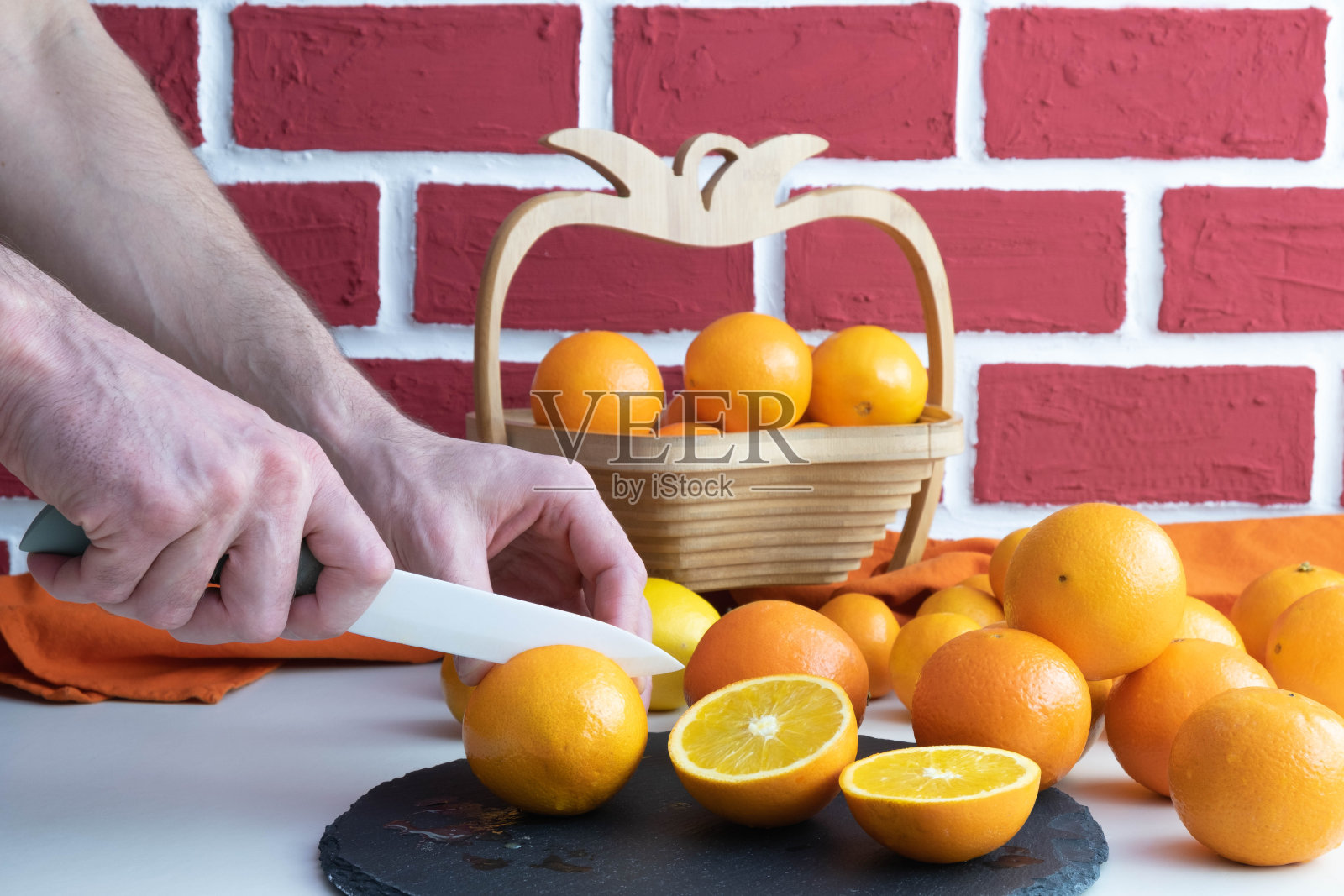 在砖墙的背景下，一名男子在桌子上切着成熟的橙子喝果汁照片摄影图片