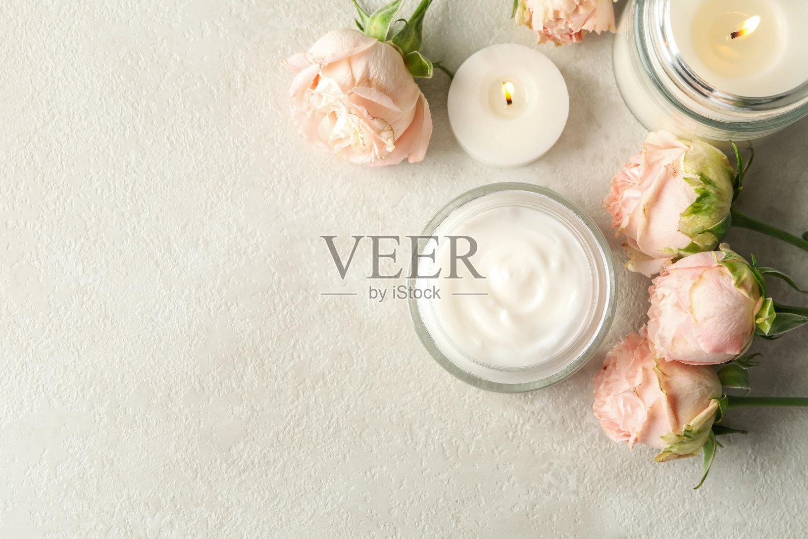 白色的桌子上放着香薰蜡烛、化妆霜和玫瑰照片摄影图片