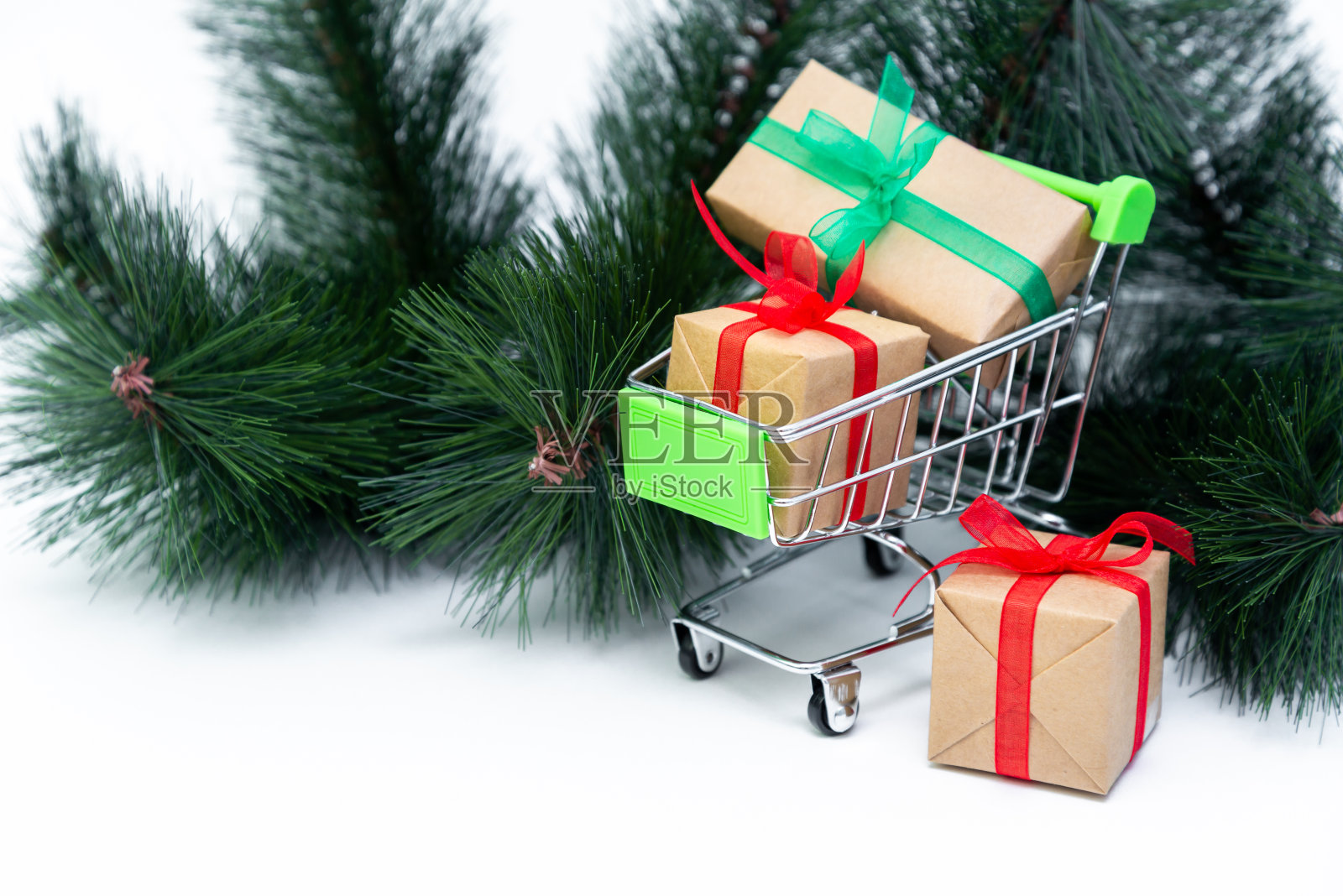 小推车与礼物盒在白色背景与圣诞树。网上购物。新年的节日促销和折扣。零售和批发采购。交易业务。副本的空间。照片摄影图片