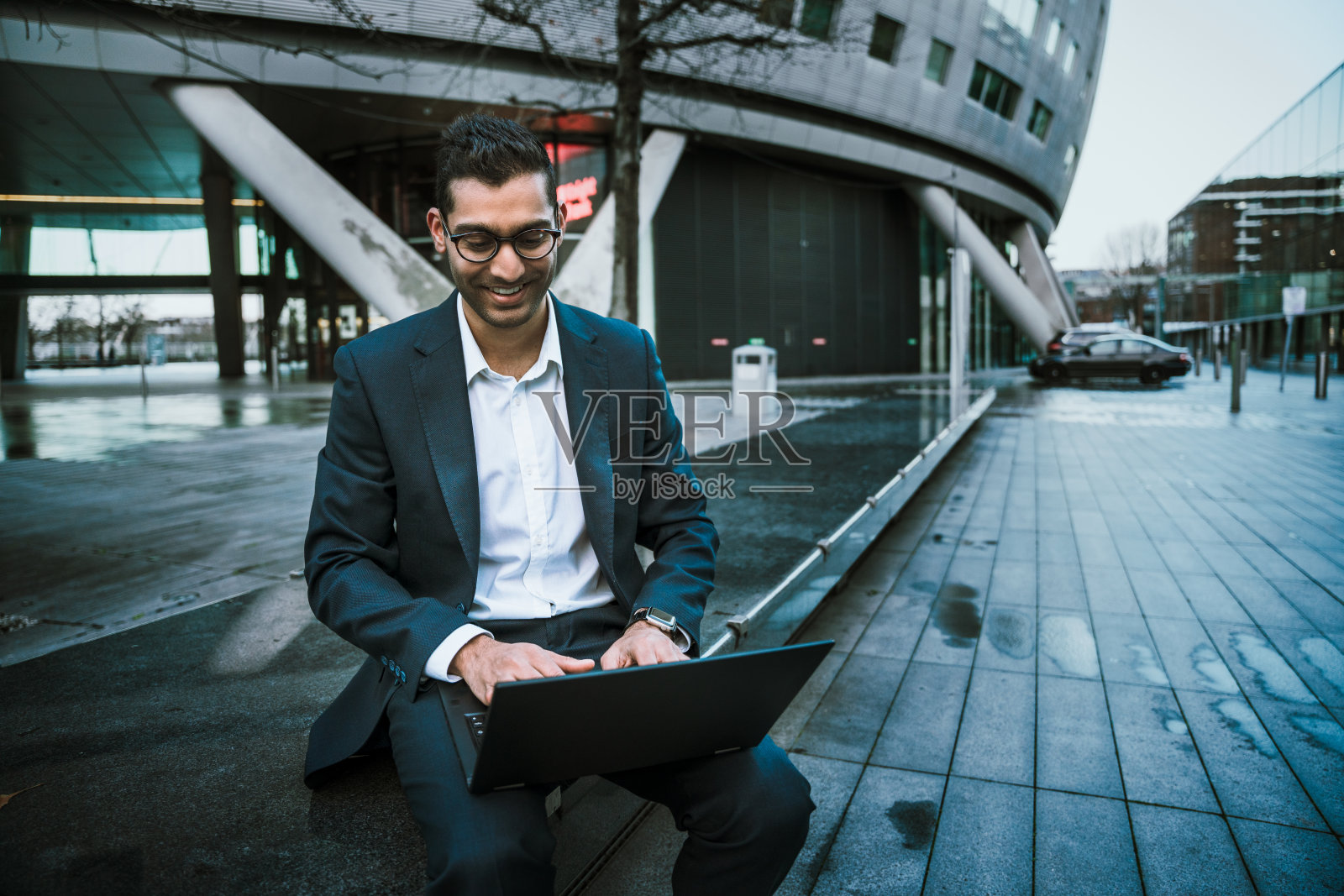 混血儿商人在笔记本电脑上打字，在漫长的一天工作后微笑照片摄影图片