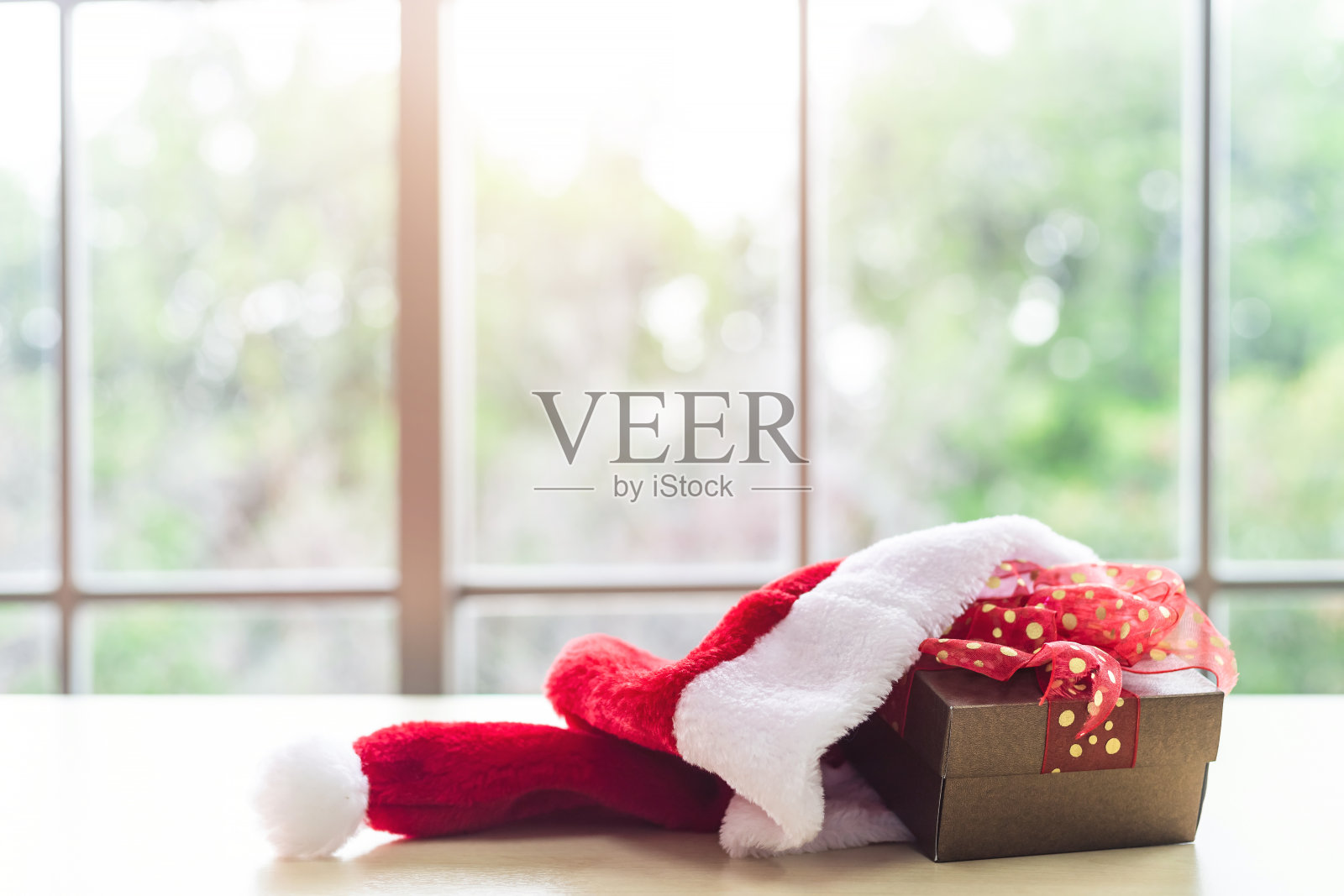 圣诞老人的帽子与礼盒放置在木制的桌子室内透过窗户与树的背景与复制空间，装饰在圣诞节和新年。照片摄影图片