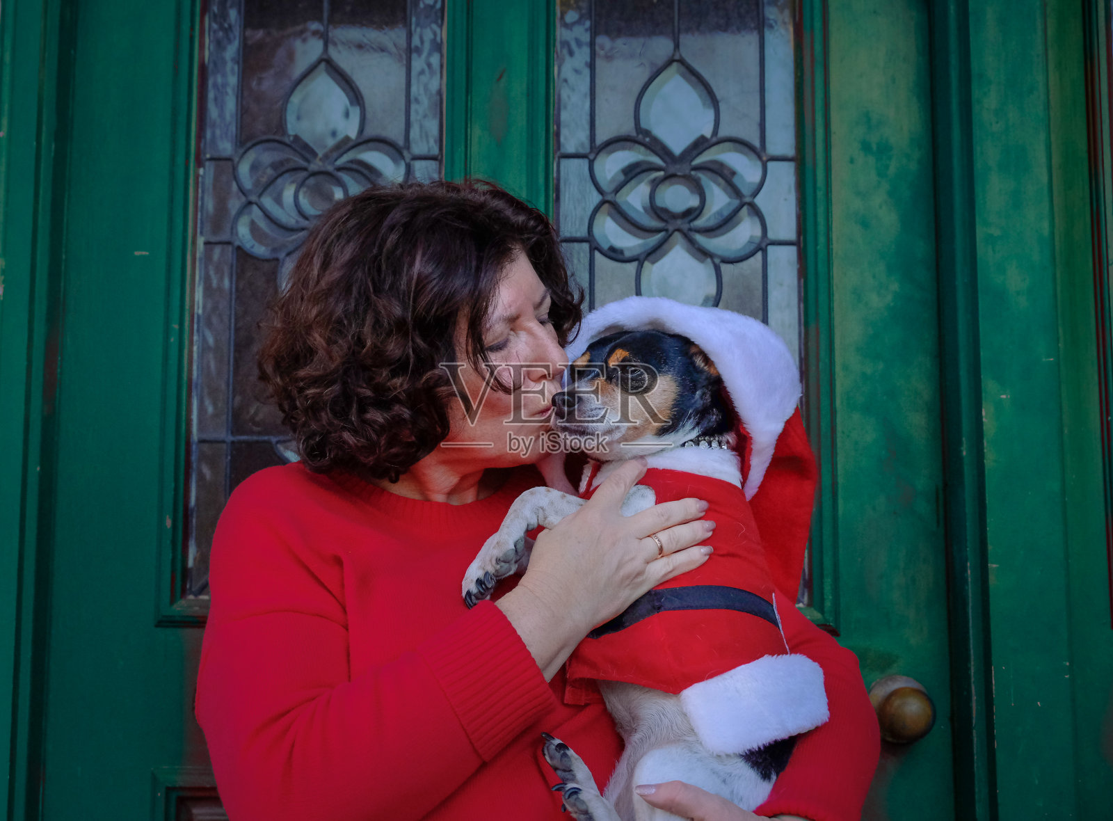 一个成熟的女人亲吻她为圣诞节打扮的狗照片摄影图片