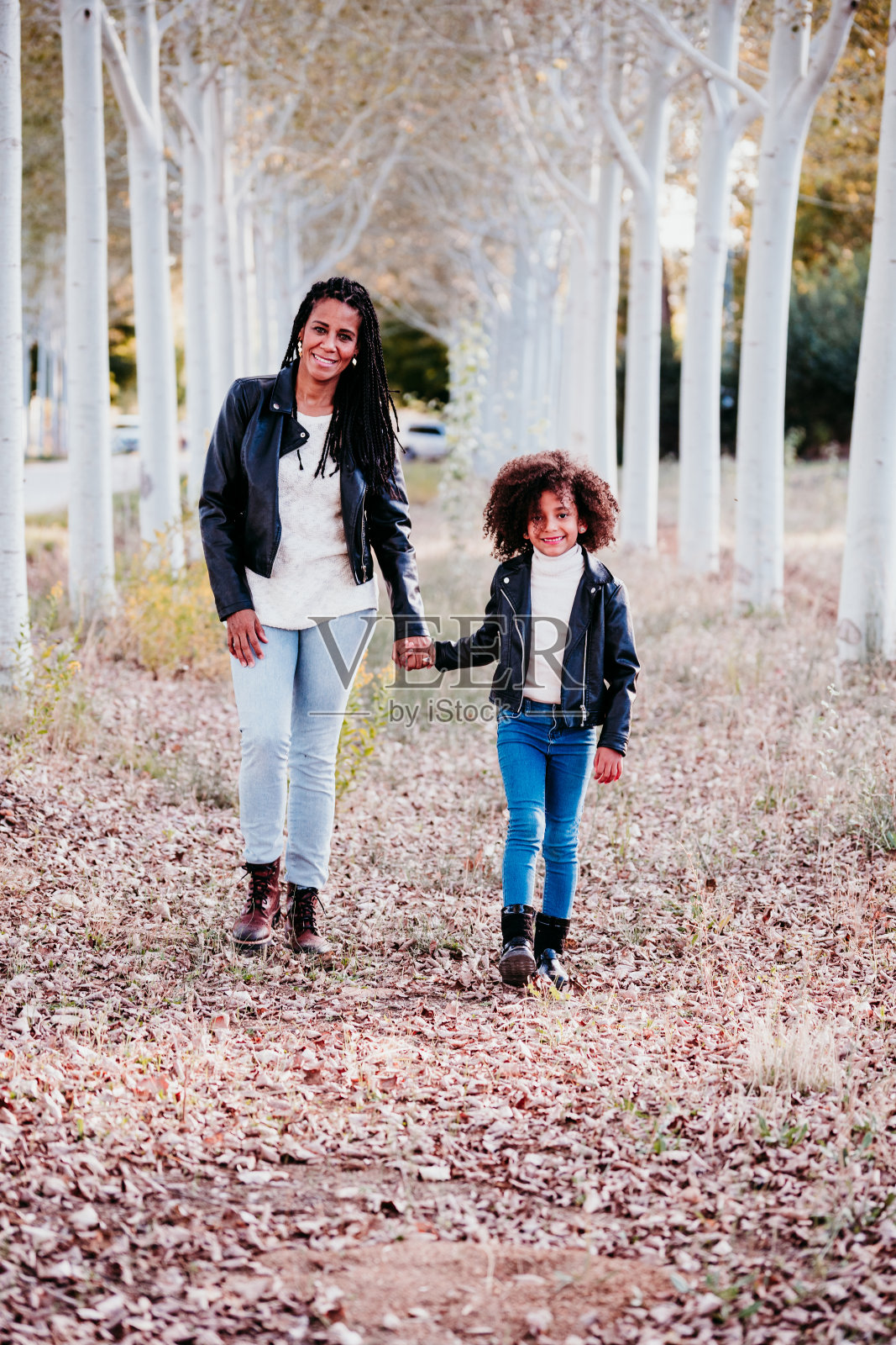 西班牙裔母亲和爆炸的孩子女孩在户外散步在日落的路径树木。秋天的季节。家庭和爱的概念照片摄影图片