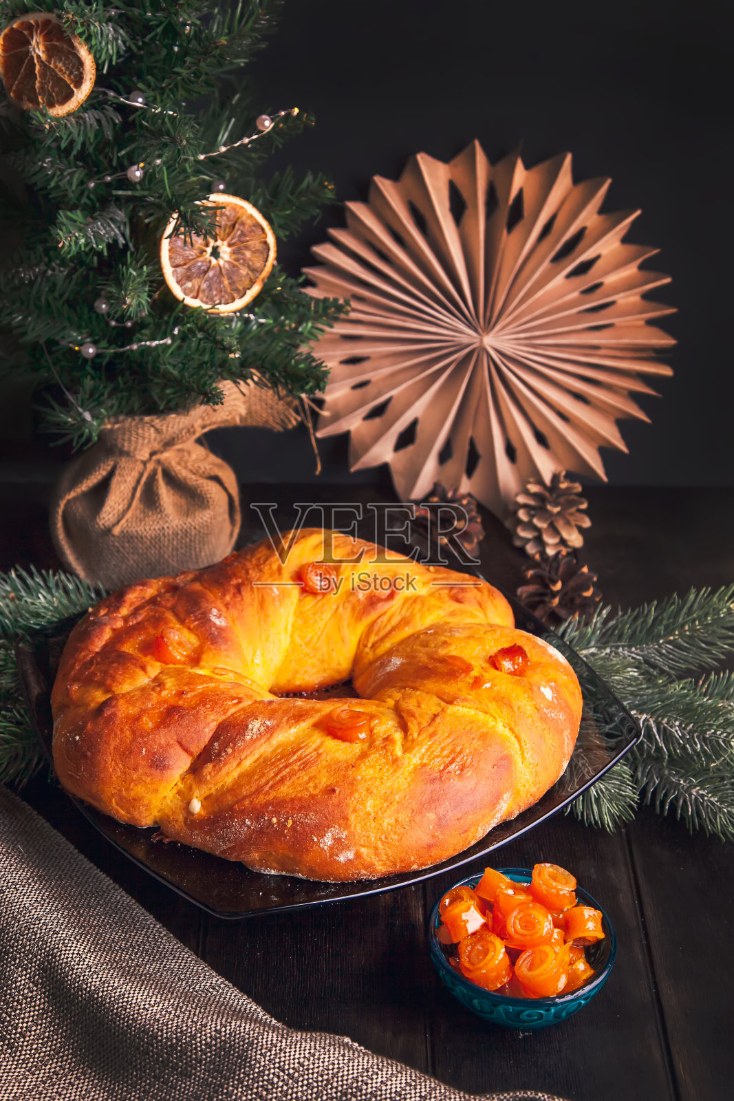 家里烤的圣诞面包在一个形状的圣诞花环酵母面团与橙色蜜饯水果在圣诞树的背景照片摄影图片