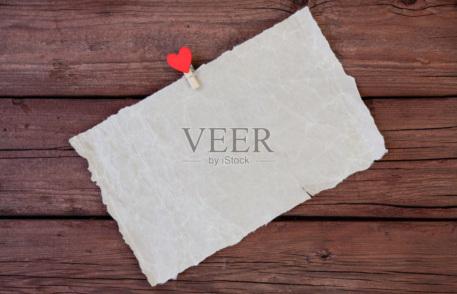 一张羊皮纸，上面有晾衣夹，木制背景上有一颗红心。副本的空间照片摄影图片