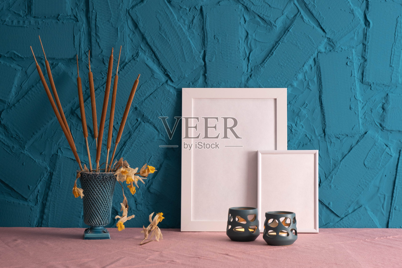 烛台上燃烧着蜡烛，装饰着芦苇圆锥体，白色框架的照片站在桌子上，在蓝色的背景照片摄影图片