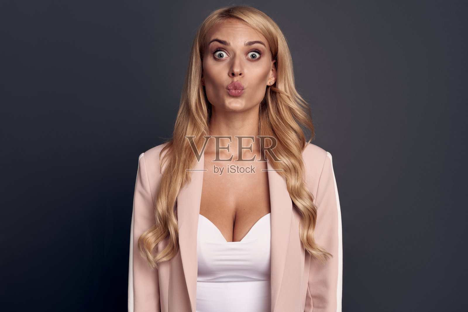 调情的年轻女子的肖像在粉红色的套装看相机和飞吻孤立在灰色的背景照片摄影图片