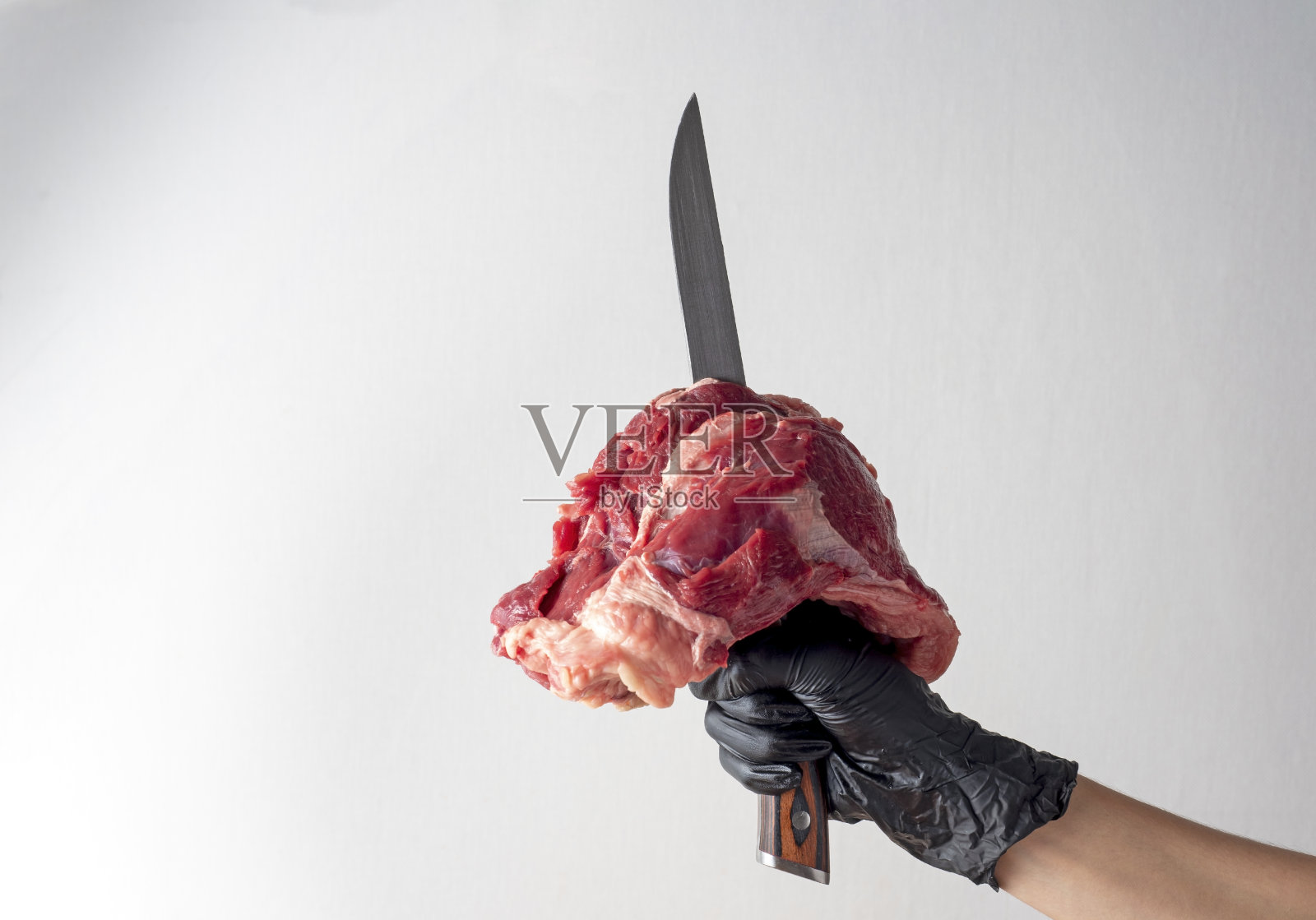 手里的刀刺着一块生牛肉孤立在白色的背景上。拷贝空间，正面视图。新鲜的肉照片摄影图片