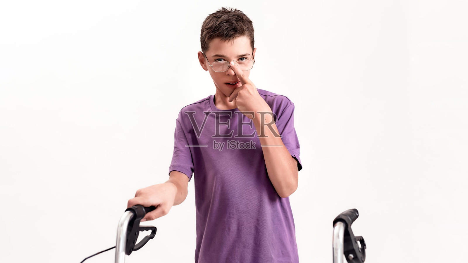患有脑瘫的残疾青少年男孩看着镜头，扶着助行器走路，白色背景照片摄影图片