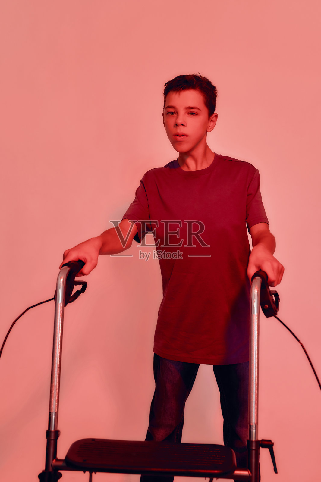 患有脑瘫的残疾少年肖像，使用助行器在红色背景下行走照片摄影图片