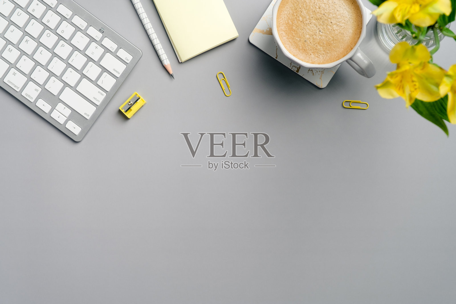 平躺，俯视图办公桌桌。工作空间有一杯咖啡、键盘、黄色办公用品和灰色背景上的花。简约风格的自由职业者工作场所。照片摄影图片