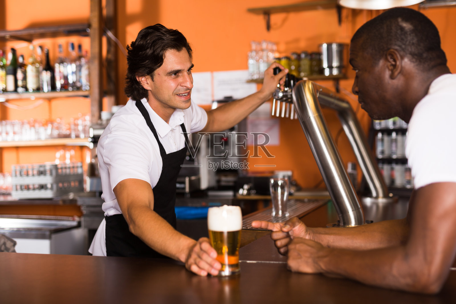 微笑的男酒保给顾客一杯金色的啤酒照片摄影图片