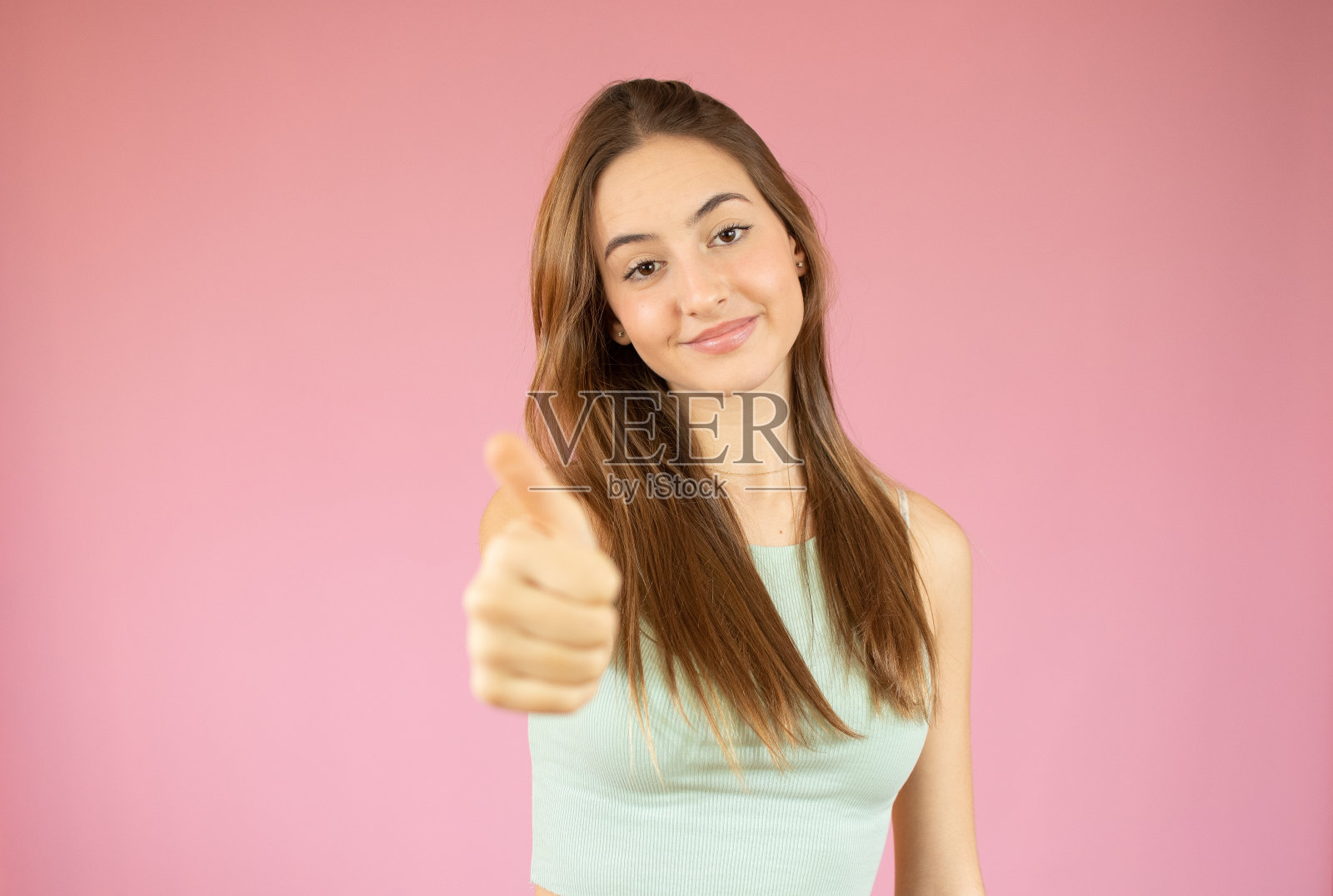 快乐的女大学生在粉红色的背景上竖起大拇指照片摄影图片