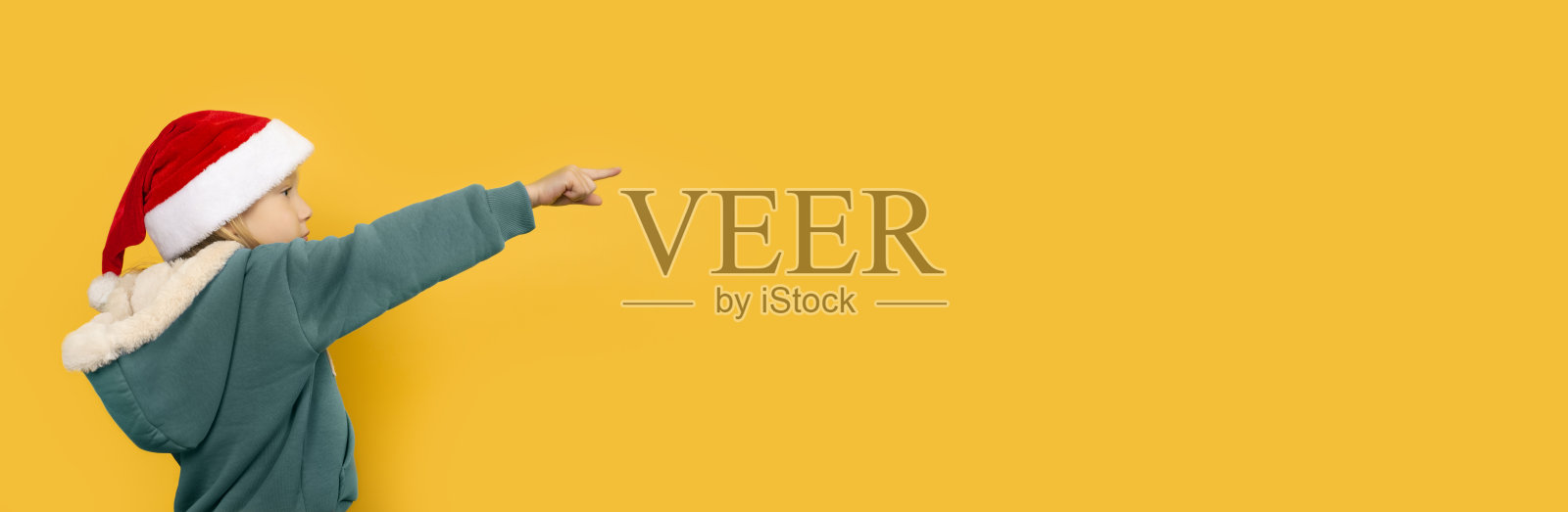 漂亮的小女孩戴着圣诞帽，微笑着指着她的手指。照片摄影图片