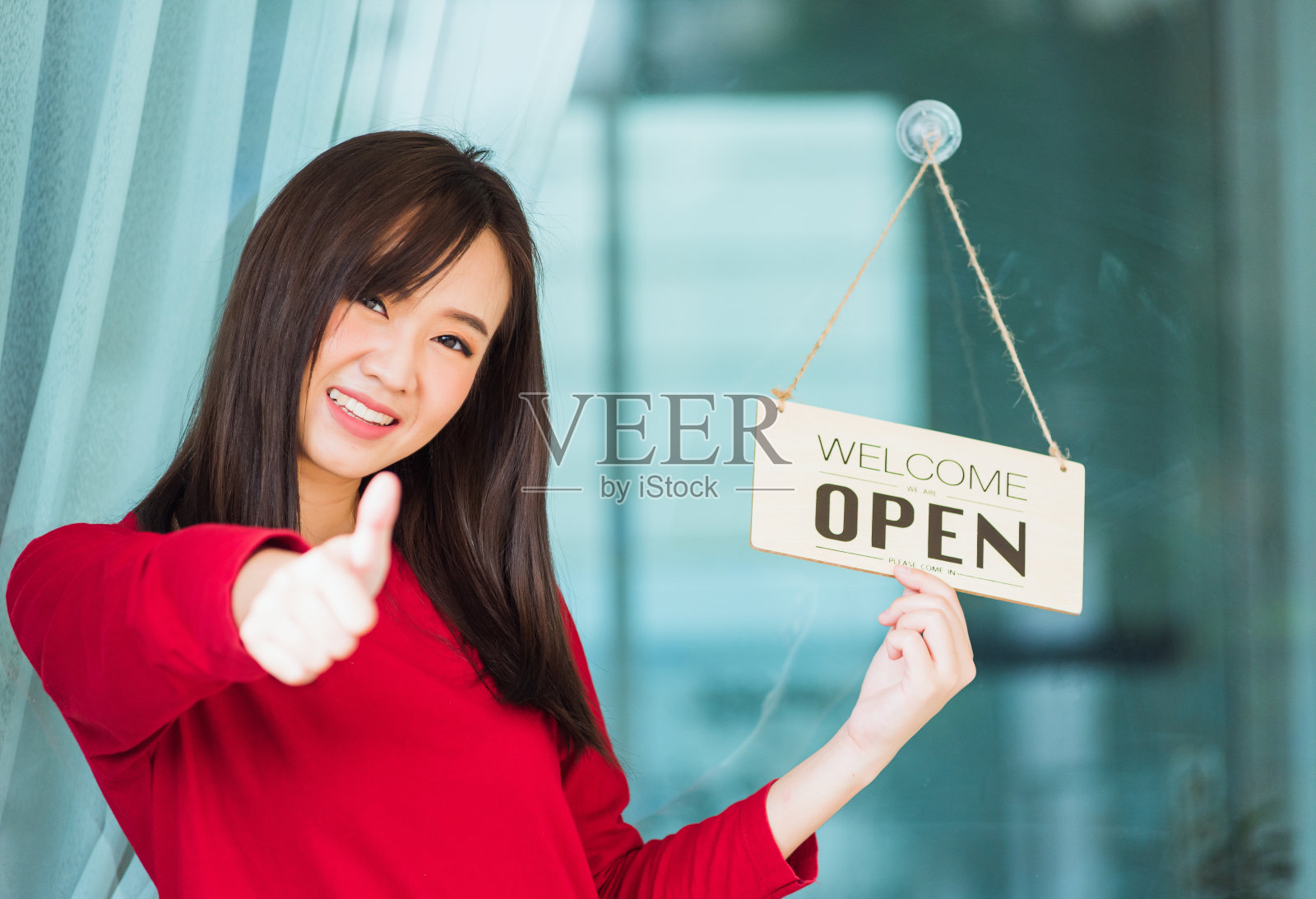 女人微笑着竖起大拇指表示她注意到一块木板上的“欢迎光临”的标签挂在玻璃门前面照片摄影图片