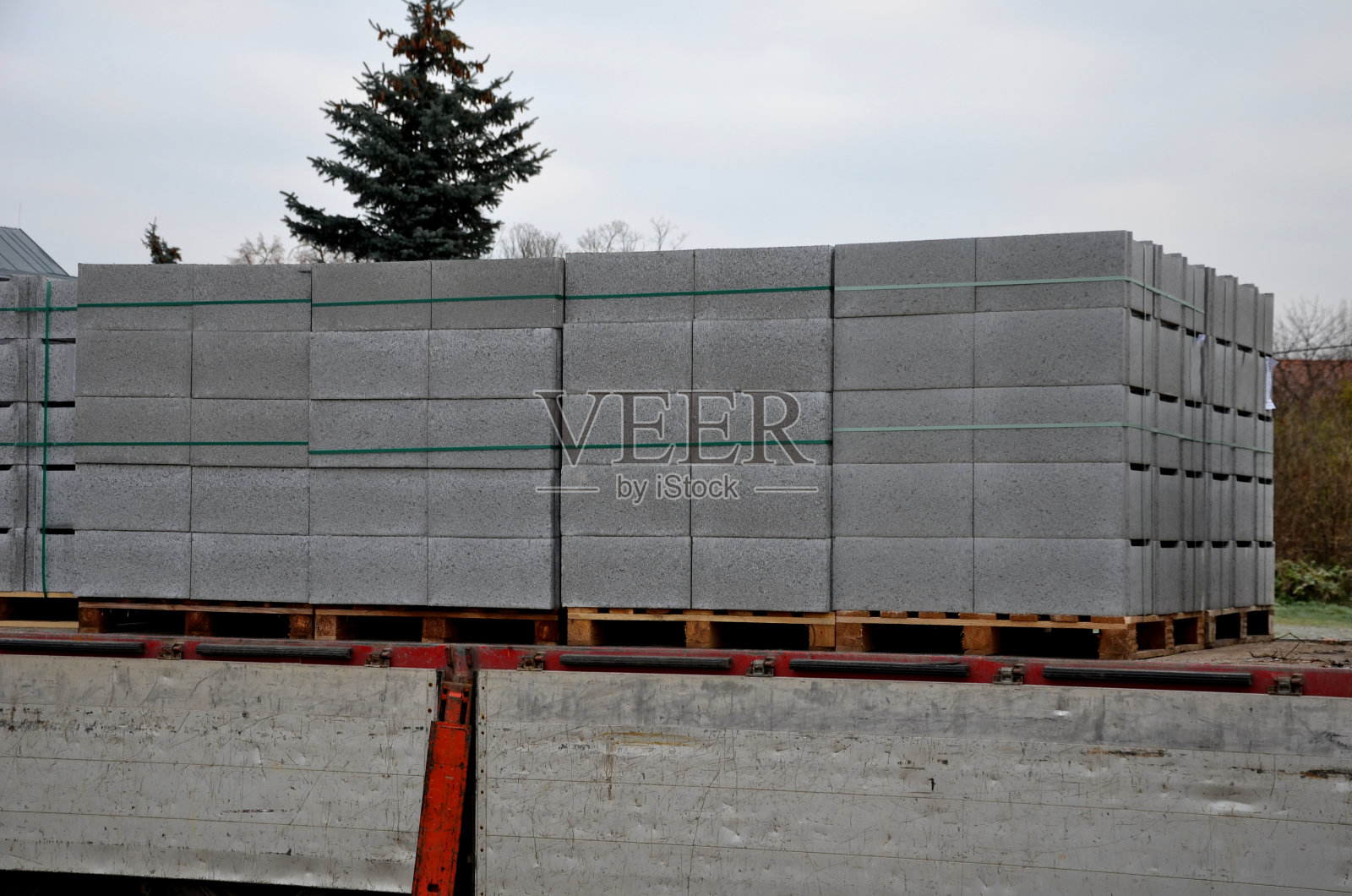 运输用于房屋地基或围栏的混凝土砖。带有灰色砖块的托盘用叉车从车身上卸下来。打开侧板，准备卸载建筑材料照片摄影图片