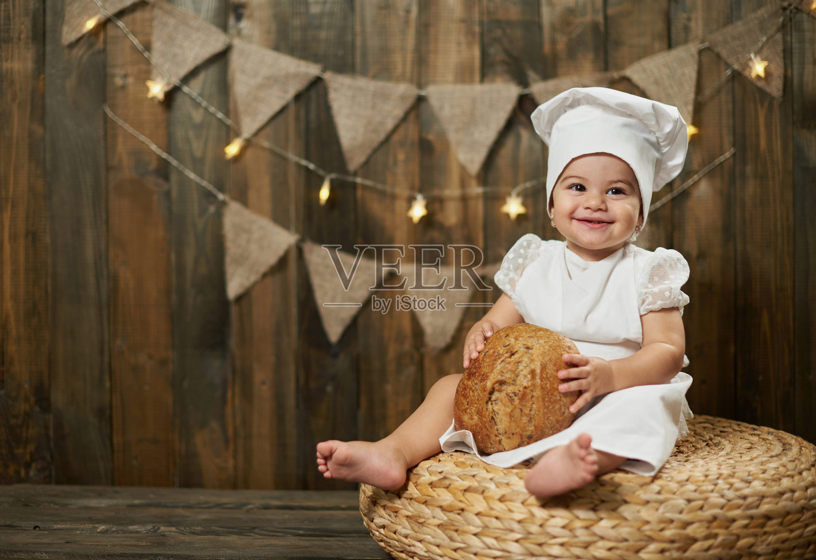在乡村木墙的背景下，小女孩面包师拿着新鲜的面包照片摄影图片