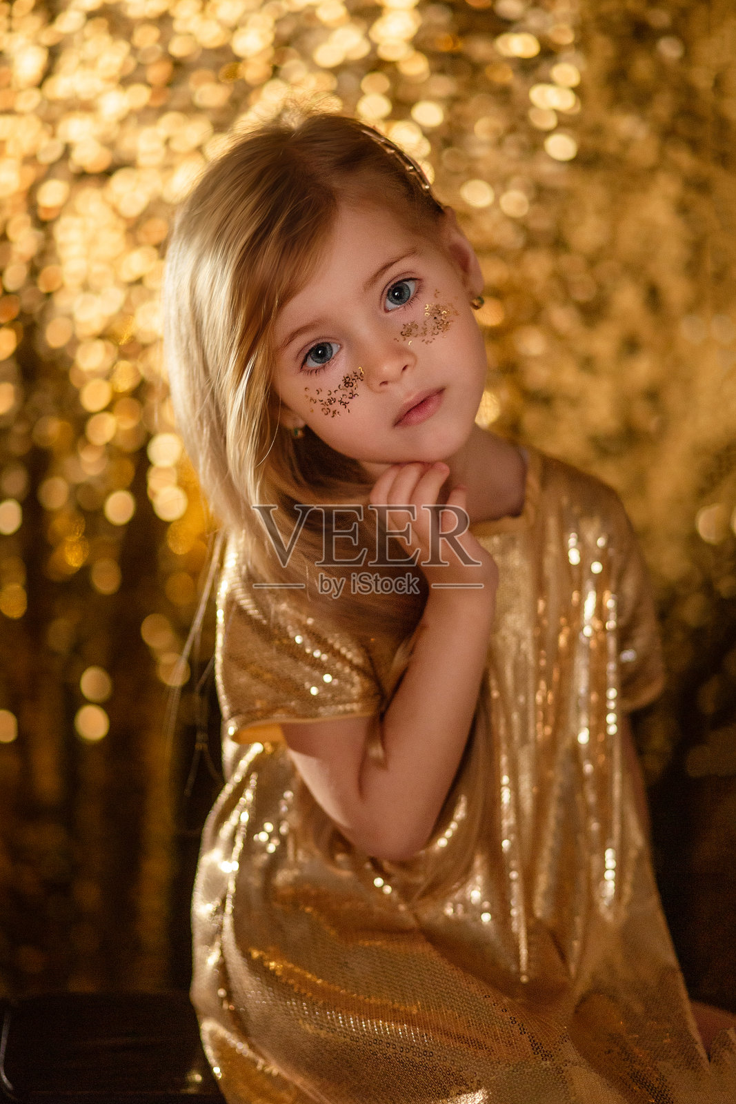 一个可爱的金发小女孩的肖像，在金色的散焦背景金色长裙。照片摄影图片