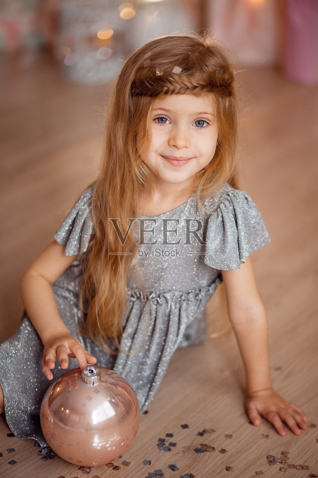 一个美丽的漂亮的女孩的肖像与长长的金发和蓝色的眼睛在金黄的散焦背景与圣诞球在她的手。照片摄影图片