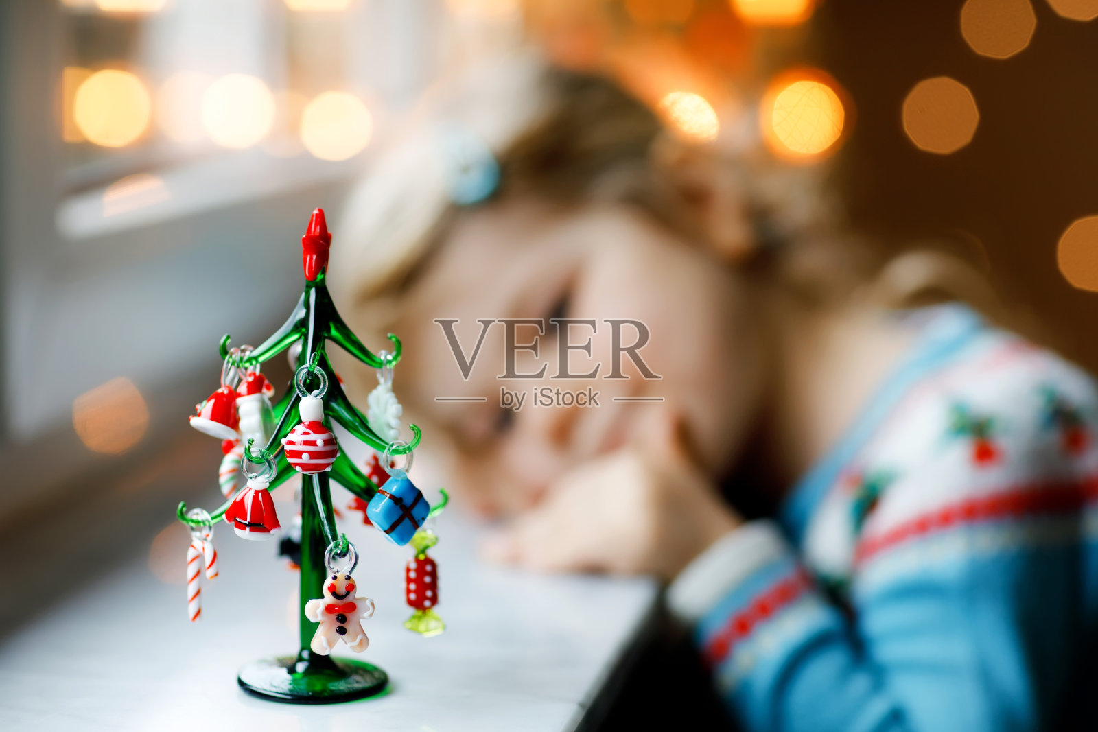 小女孩坐在窗边，用小小的圣诞玩具装饰小玻璃圣诞树。快乐健康的孩子庆祝家庭传统节日。可爱的婴儿。选择关注树照片摄影图片