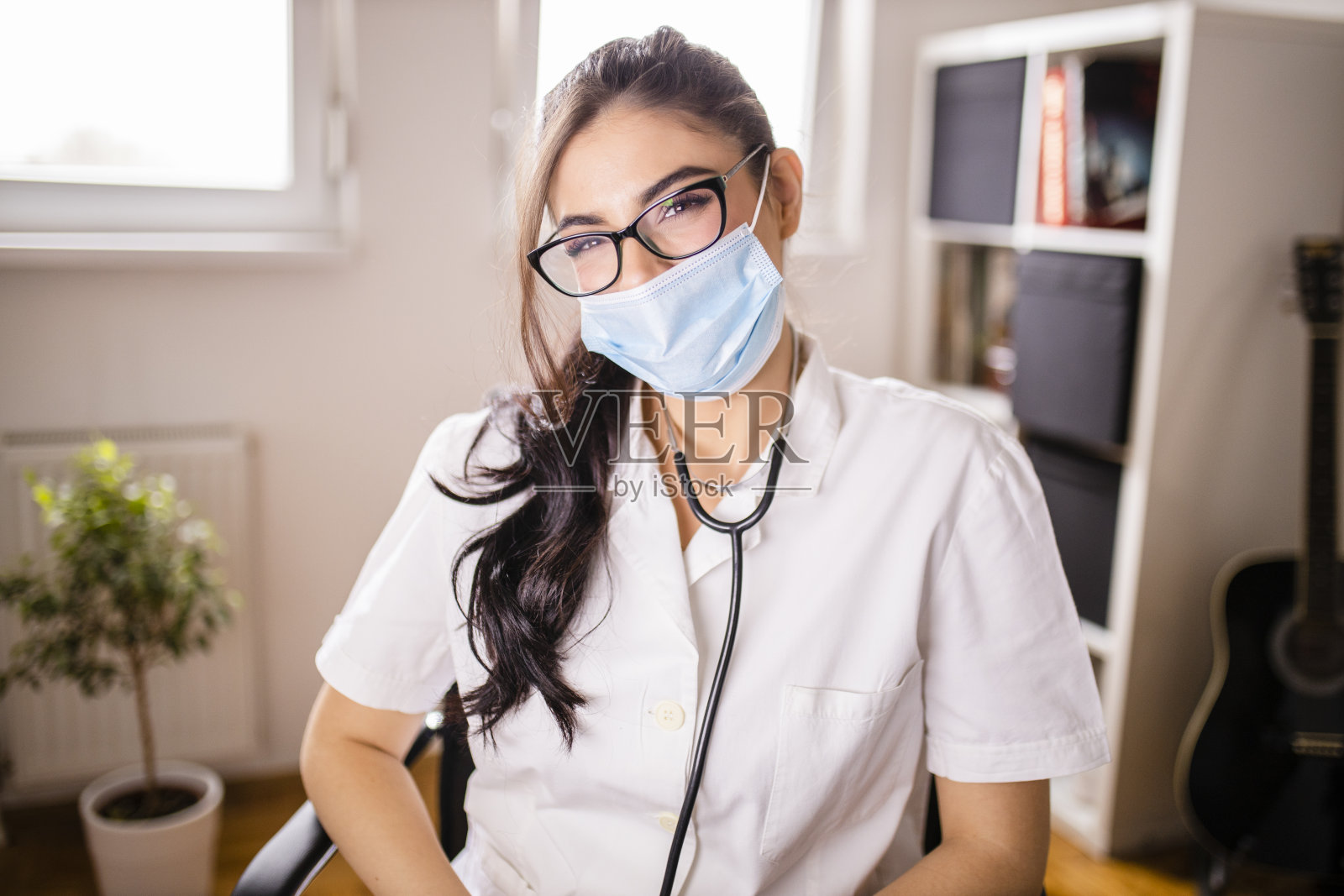 年轻女医生的肖像戴着防护面罩和听诊器在她的办公室照片摄影图片