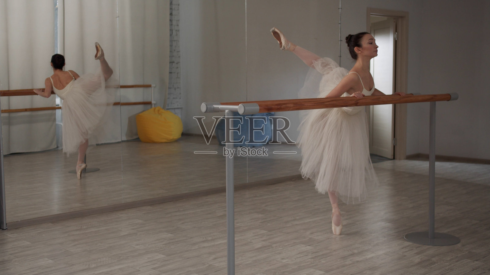 有抱负的芭蕾舞演员穿着戏服在芭蕾舞大厅里为双腿做热身，将它们向不同的方向移动照片摄影图片