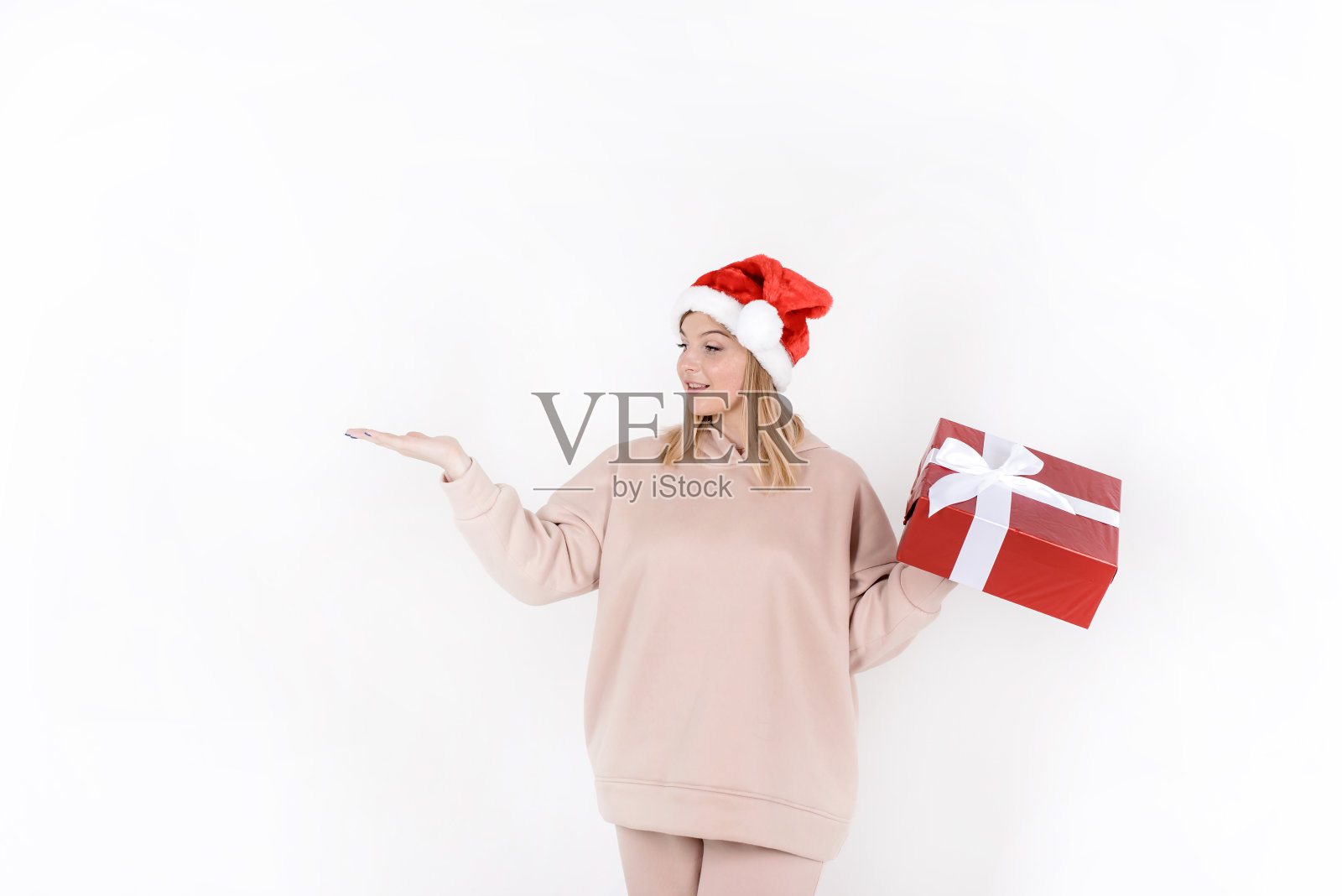 美丽快乐的女人用红色礼盒呈现你的产品与手掌，寒假气氛。女孩拿着圣诞礼物。购物销售概念照片摄影图片