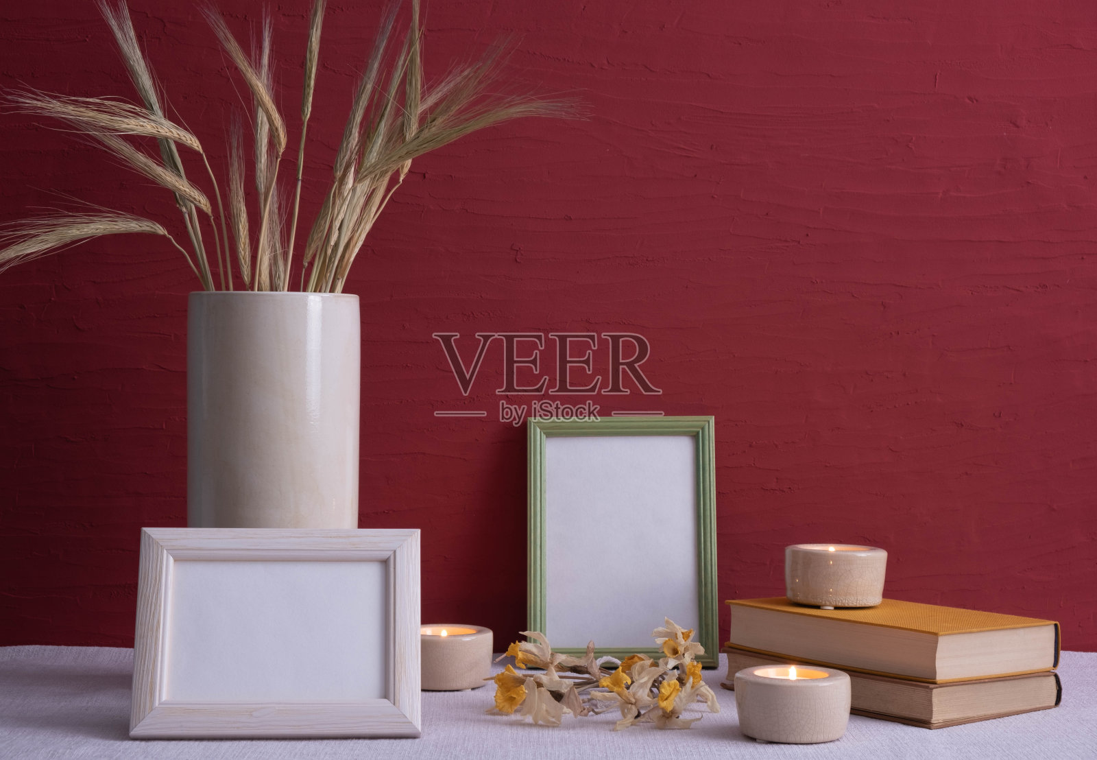 旧书，蜡烛燃烧着，一个灰色花瓶上插着玉米穗，干水仙花，桌子上有红色背景的相框照片摄影图片