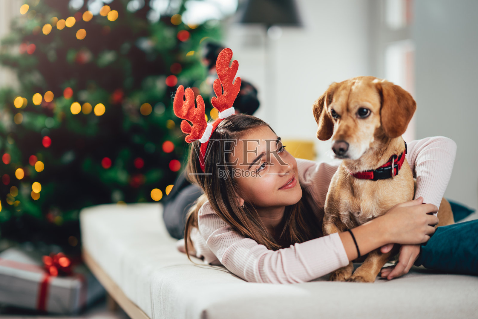 一个戴着鹿角的少女躺在床上，抱着她的狗照片摄影图片