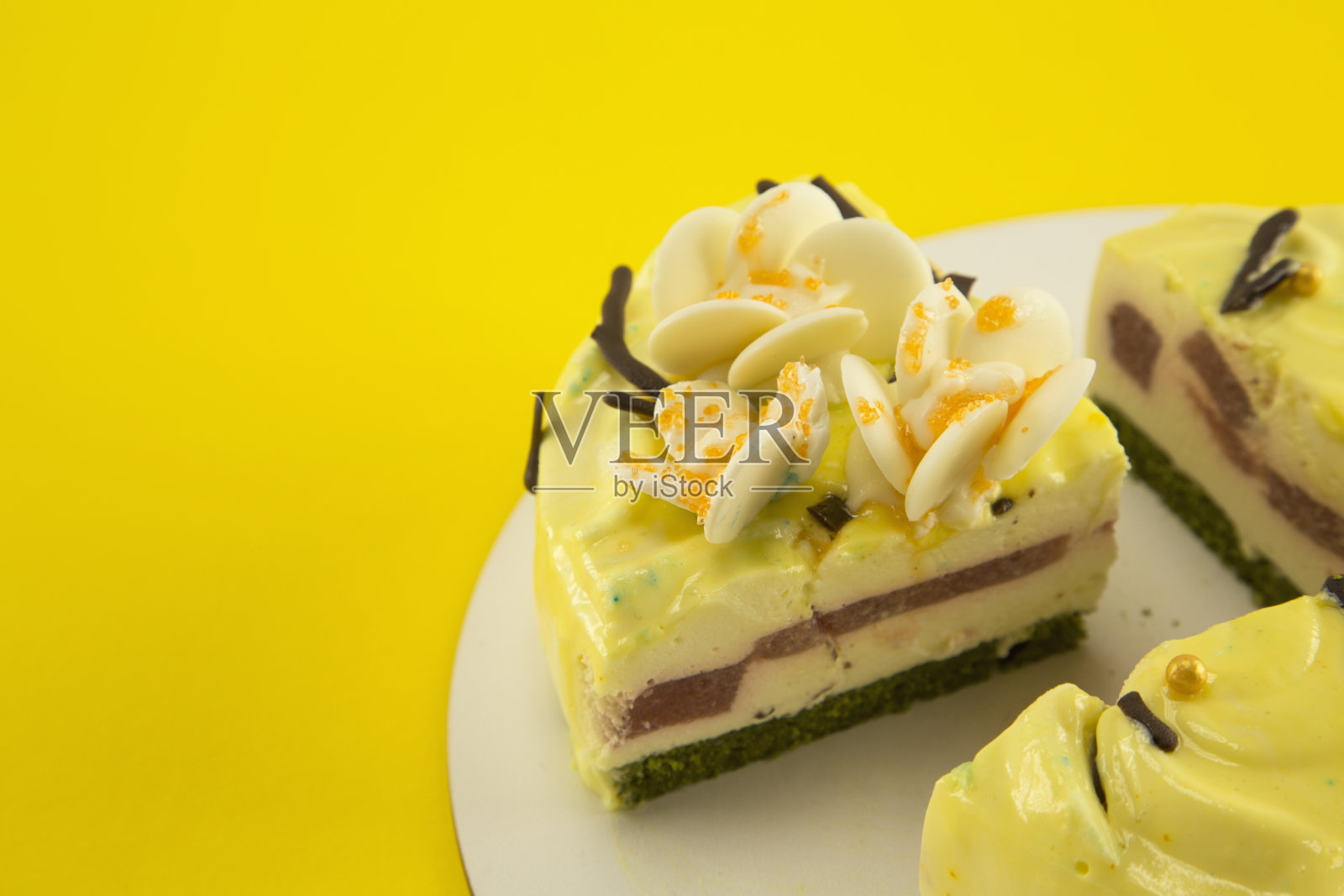 精致的柠檬色减肥蛋糕与切块薄荷海绵蛋糕，冰淇淋舒芙蕾和草莓，白色的巧克力兰花花瓣和金黄色的珍珠在黄色的背景照片摄影图片
