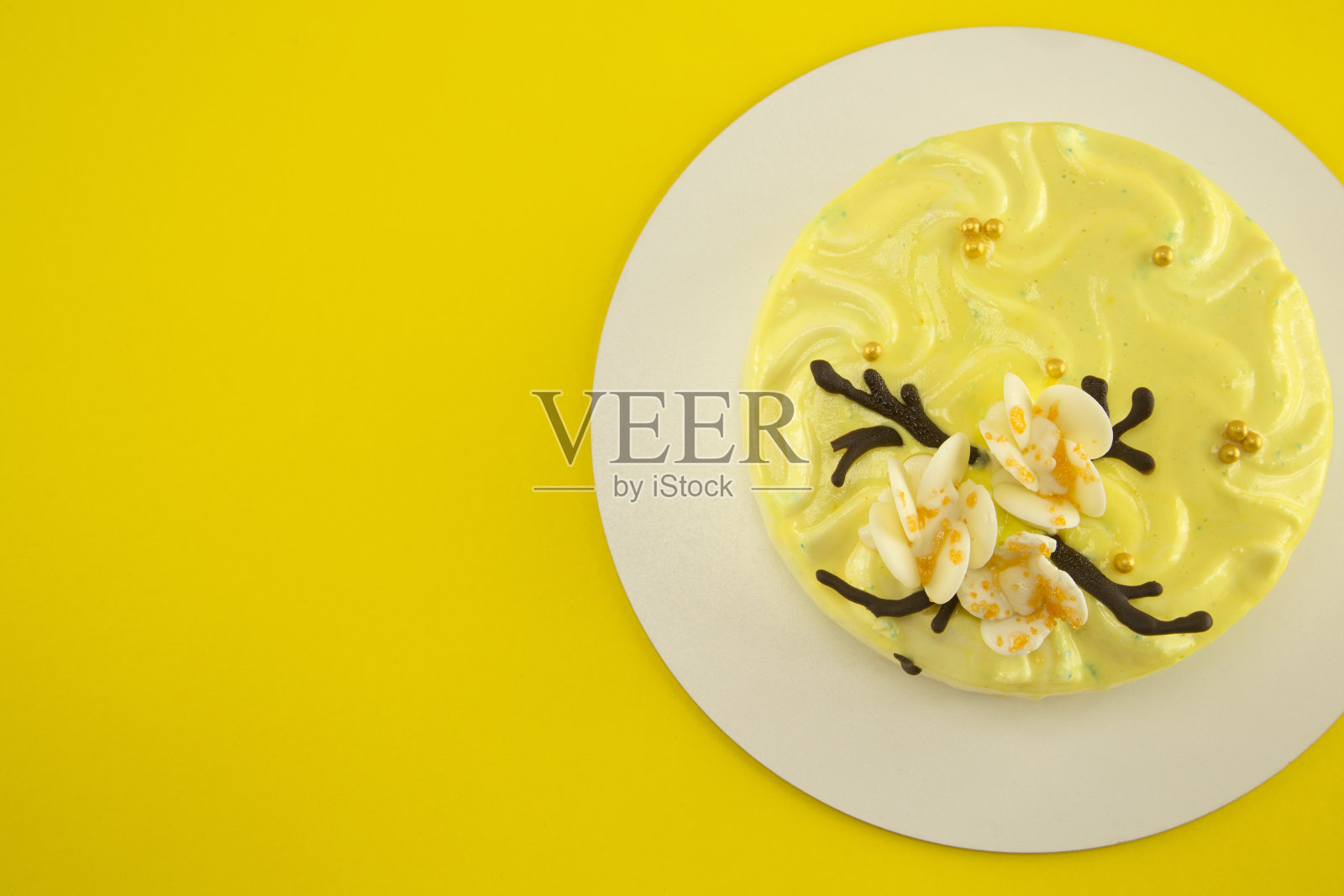 精致的柠檬色减肥蛋糕上的白色stand- mint海绵蛋糕冰淇淋soufflé和草莓confit，装饰白色巧克力兰花花瓣和金黄色的珍珠在黄色的背景照片摄影图片