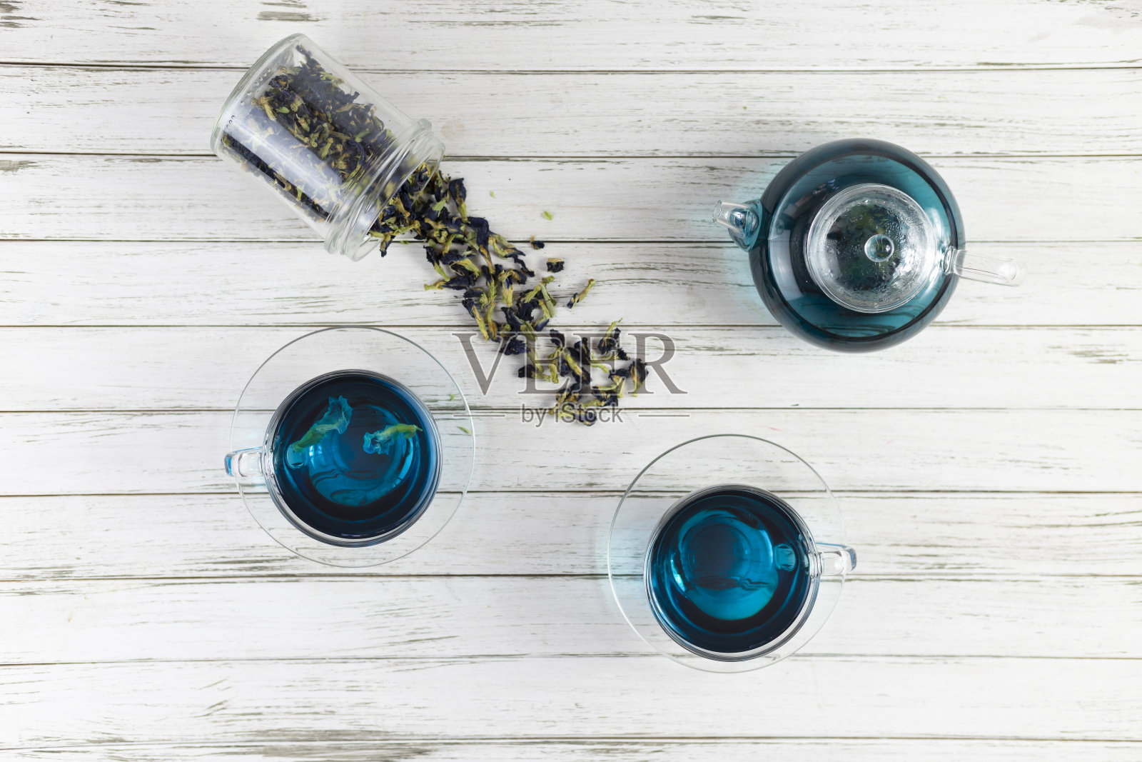 蝴蝶豌豆茶的玻璃杯和茶壶。安珊，白木背景上的阴蒂。带着一束蓝色的花。平躺照片摄影图片