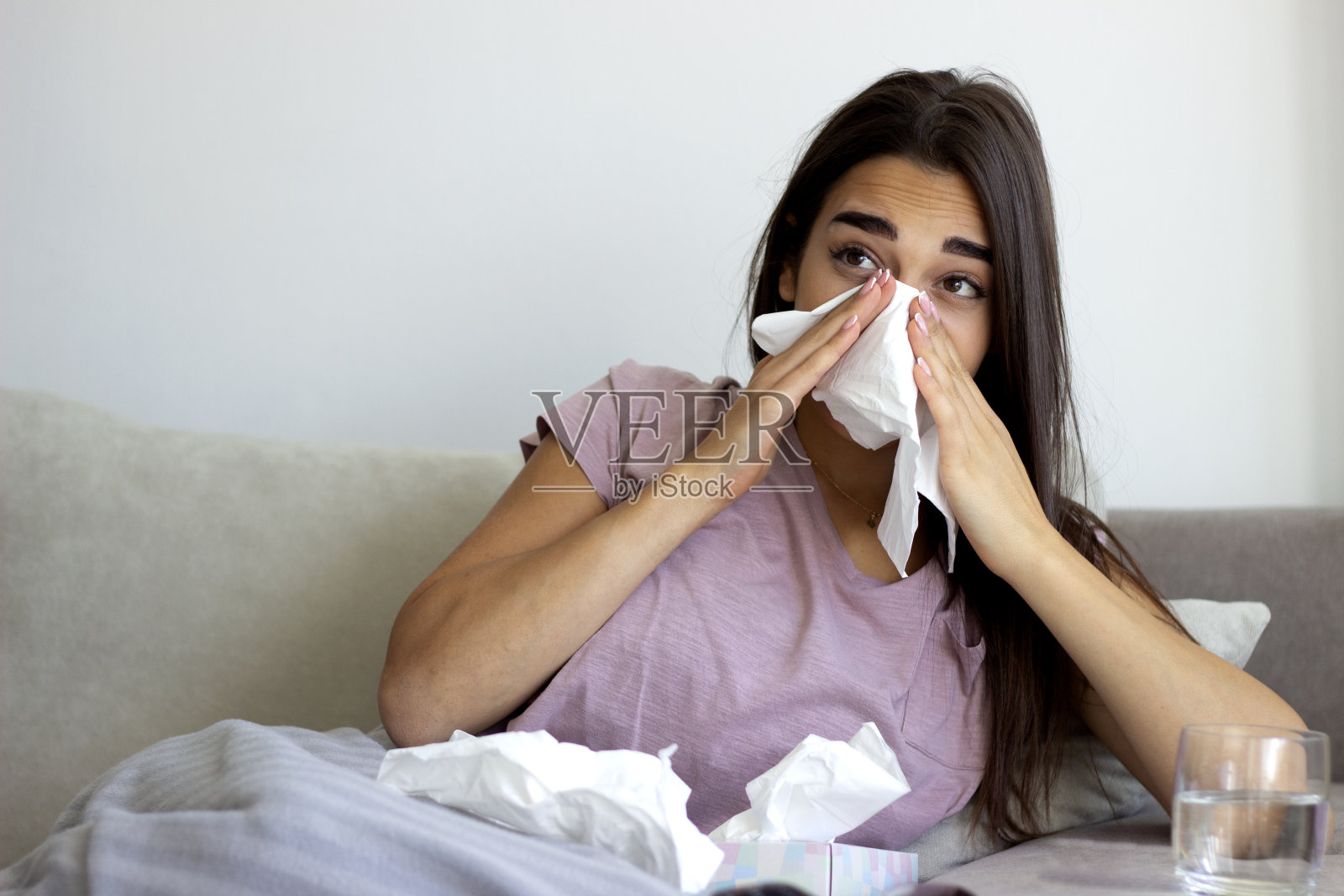生病的年轻女子因感冒躺在家里的沙发上。照片摄影图片