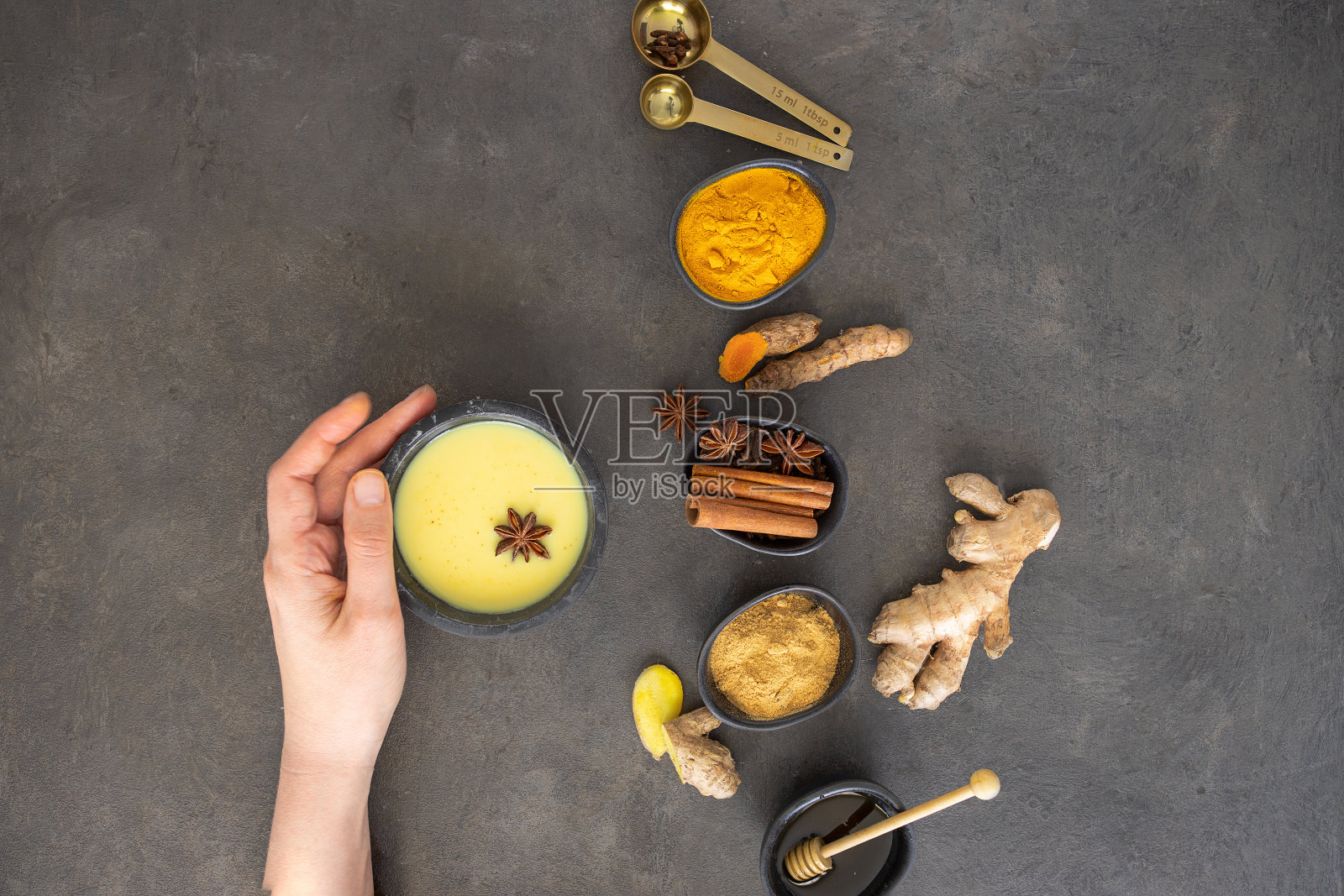 手握金杯牛奶，混凝土背景下的阿育吠陀饮料。预防疾病和增强免疫系统的自然疗法照片摄影图片