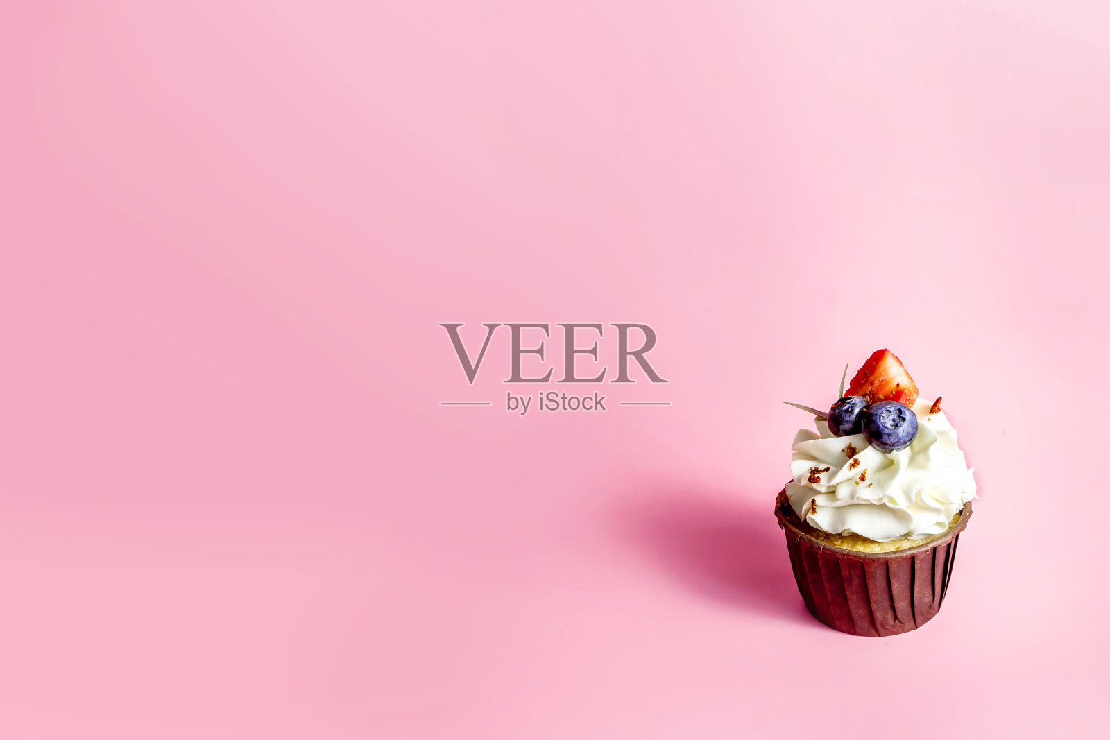 美味的纸杯蛋糕与奶油和新鲜的浆果孤立在粉红色的背景。副本的空间。照片摄影图片