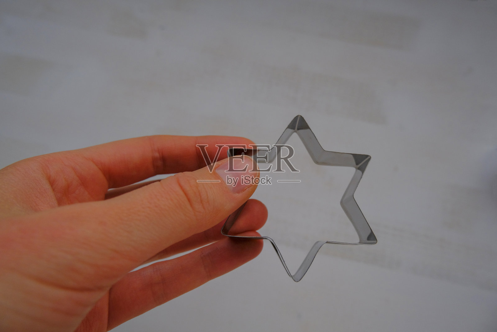 手握银色金属星形饼干切割器烘烤横跨白色木质背景俯视图。本空间照片摄影图片