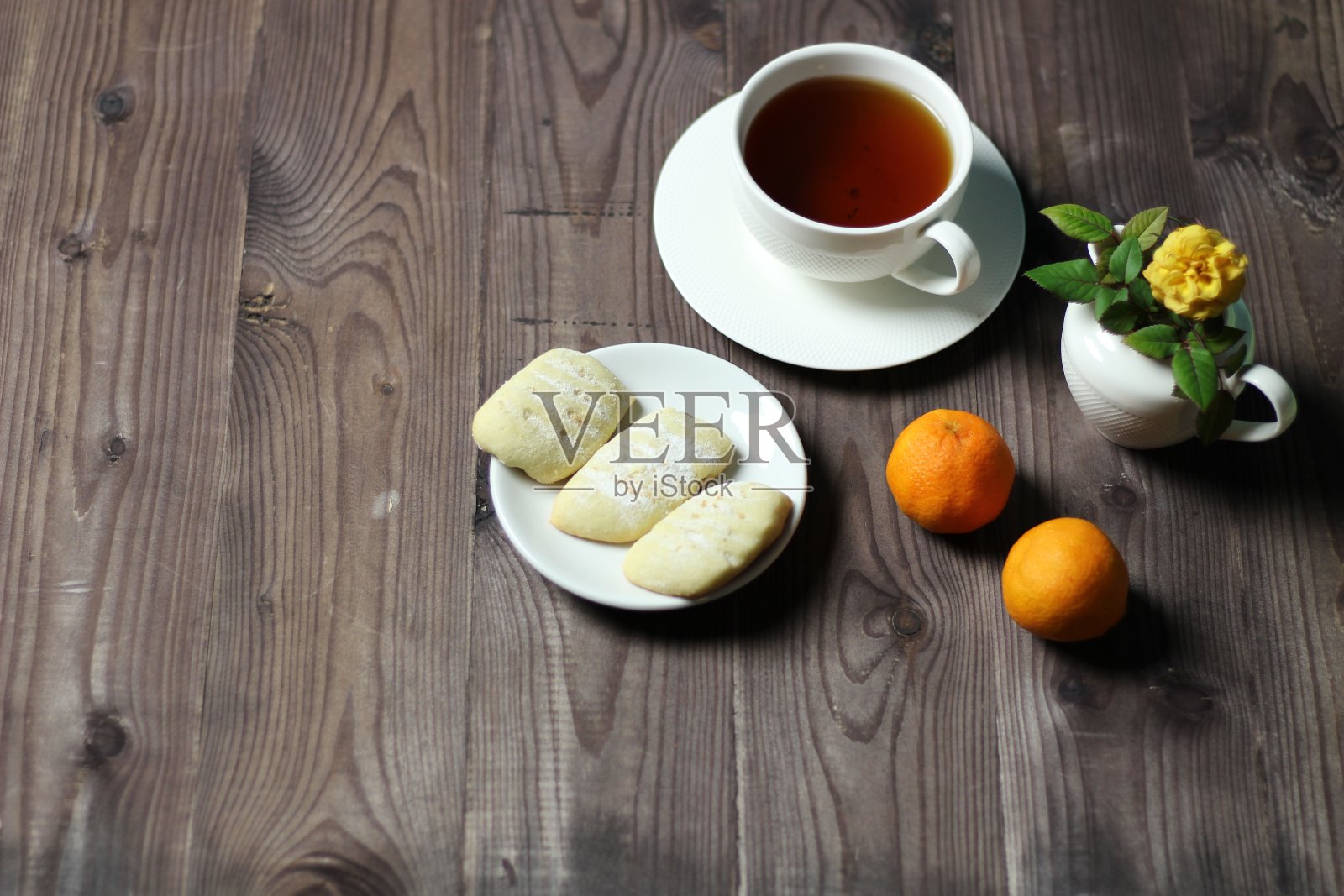 一杯茶，橘子，黄玫瑰花和饼干在棕色的木头背景照片摄影图片