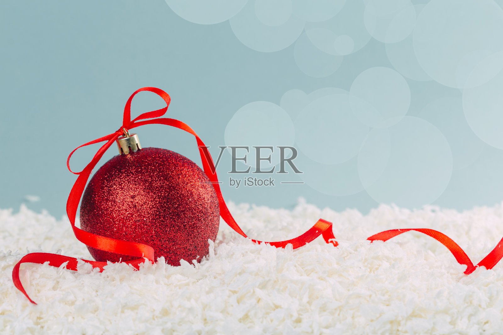 红色的圣诞球与丝带蝴蝶结在雪在蓝色的背景和散景灯。新年贺卡照片摄影图片