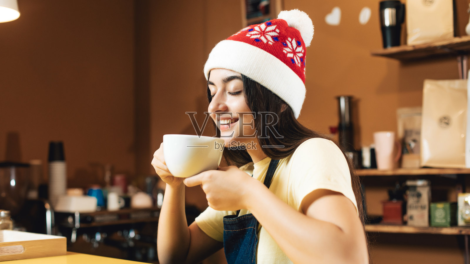 在咖啡店戴着圣诞帽做咖啡师的年轻女子。新年心情同一杯饮料。女孩正在喝咖啡照片摄影图片